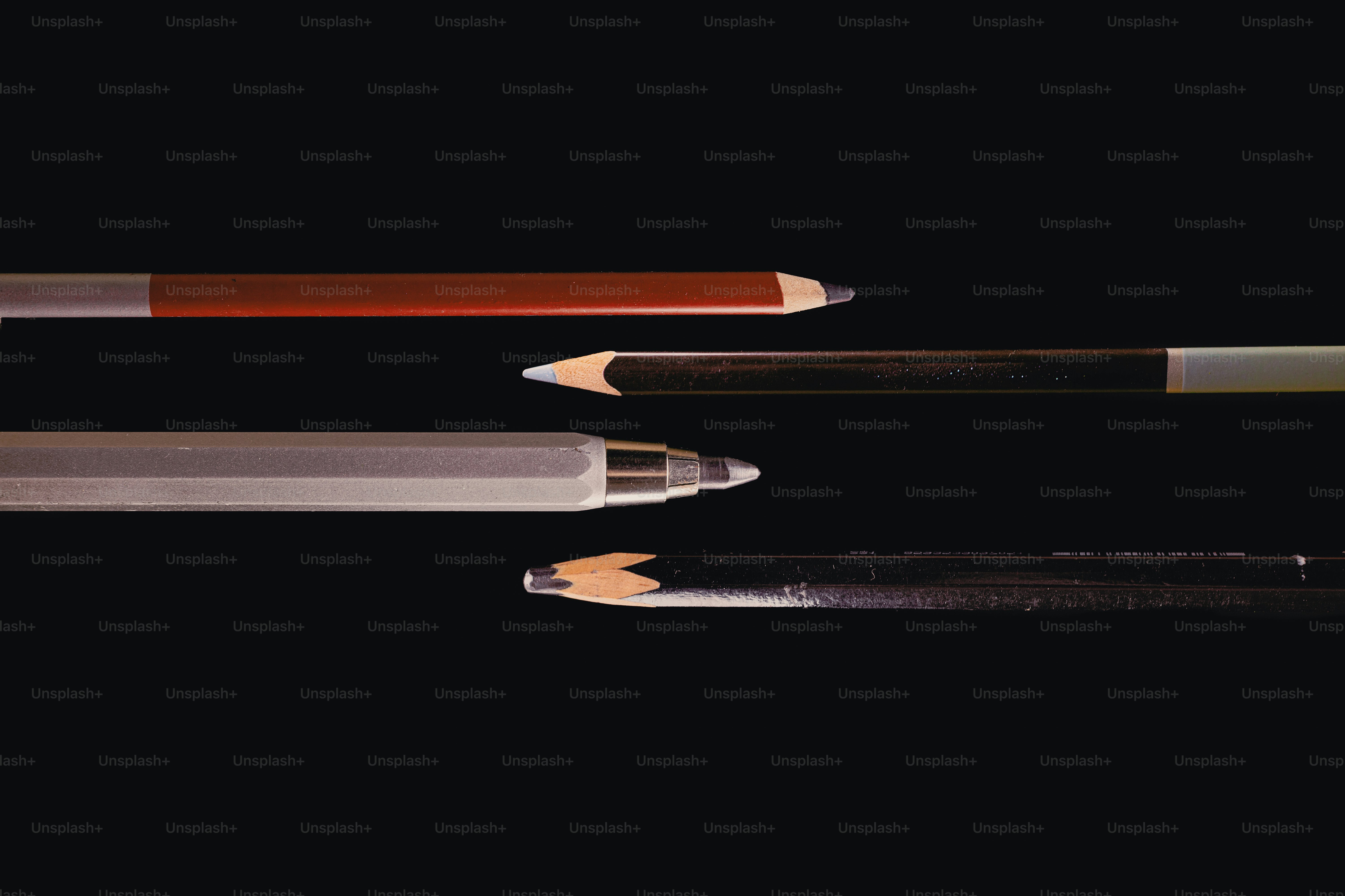 Matite assortite e una penna su uno sfondo scuro.