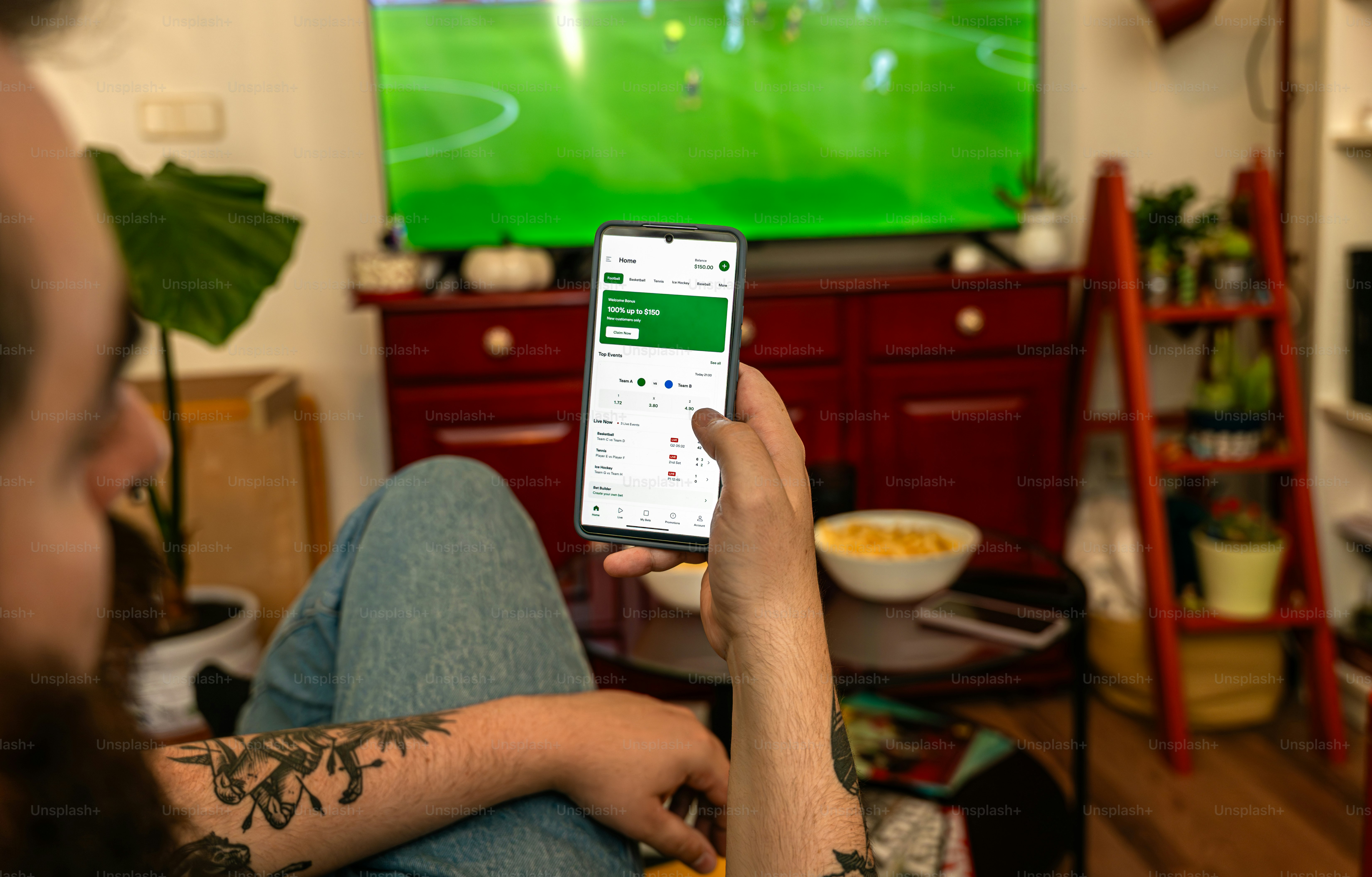 A man watches football on TV and checks his phone.