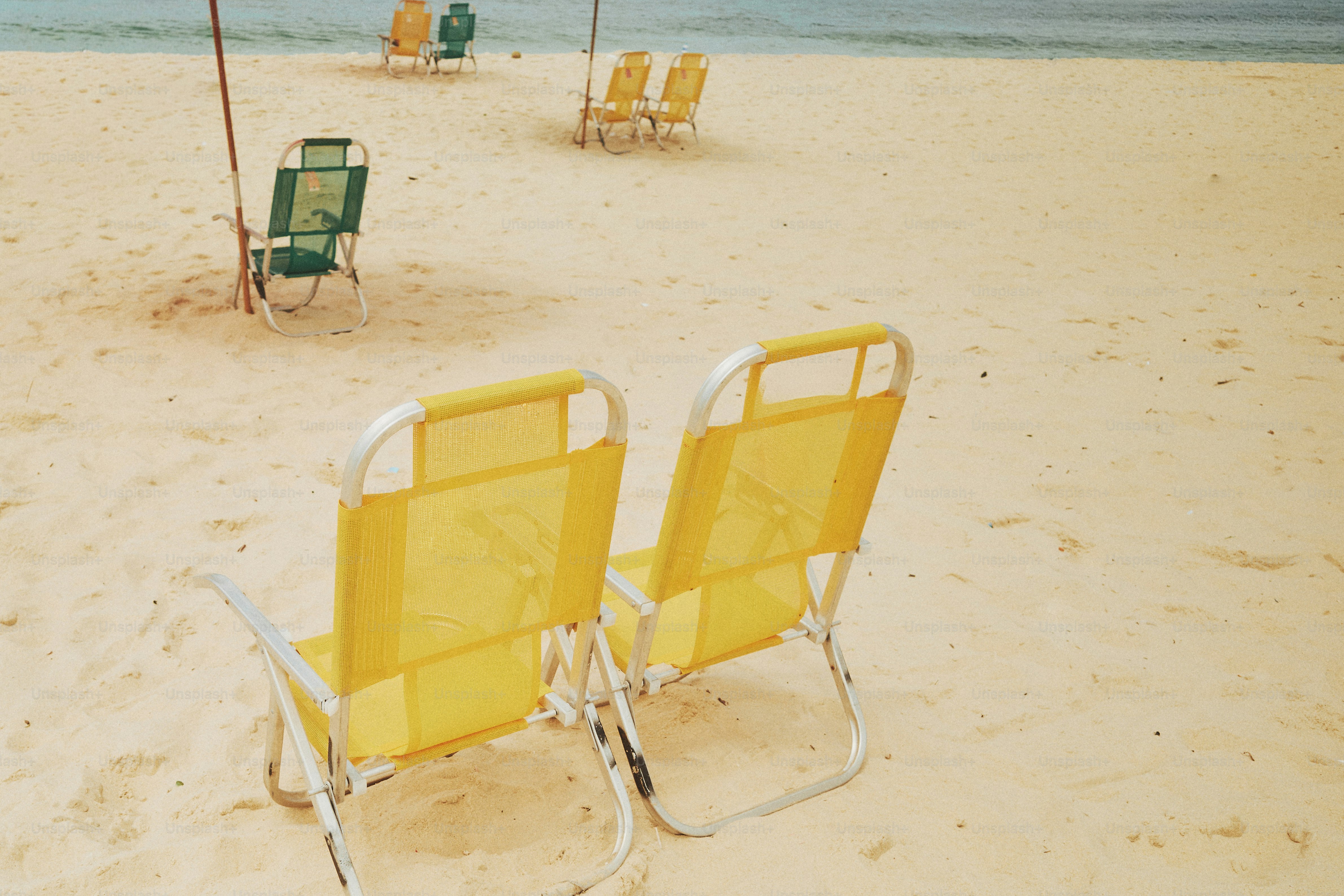 海に面した砂浜に置かれた黄色いビーチチェア。の写真 – Unsplashの浜