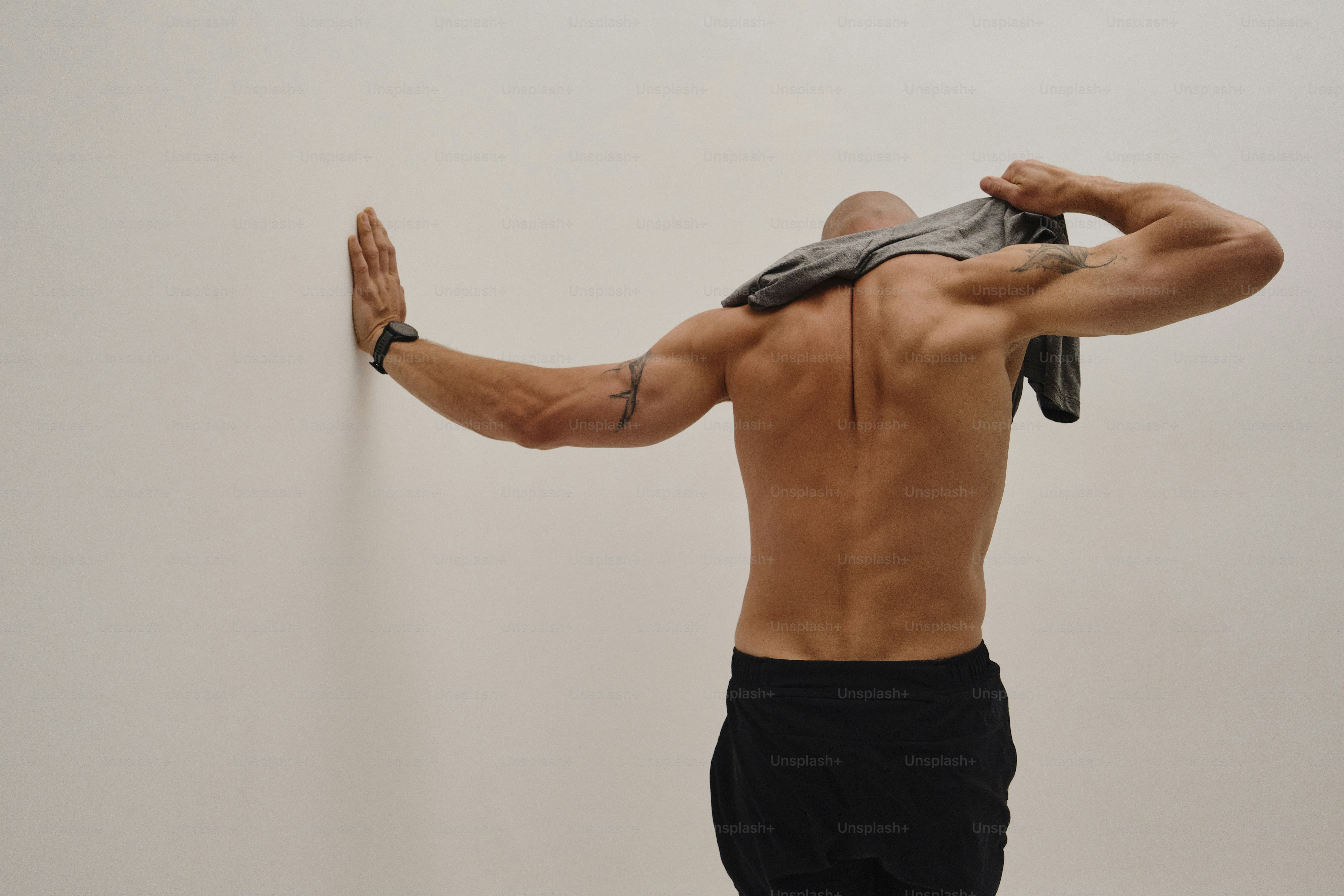 Muscular man taking off his shirt against a white wall.