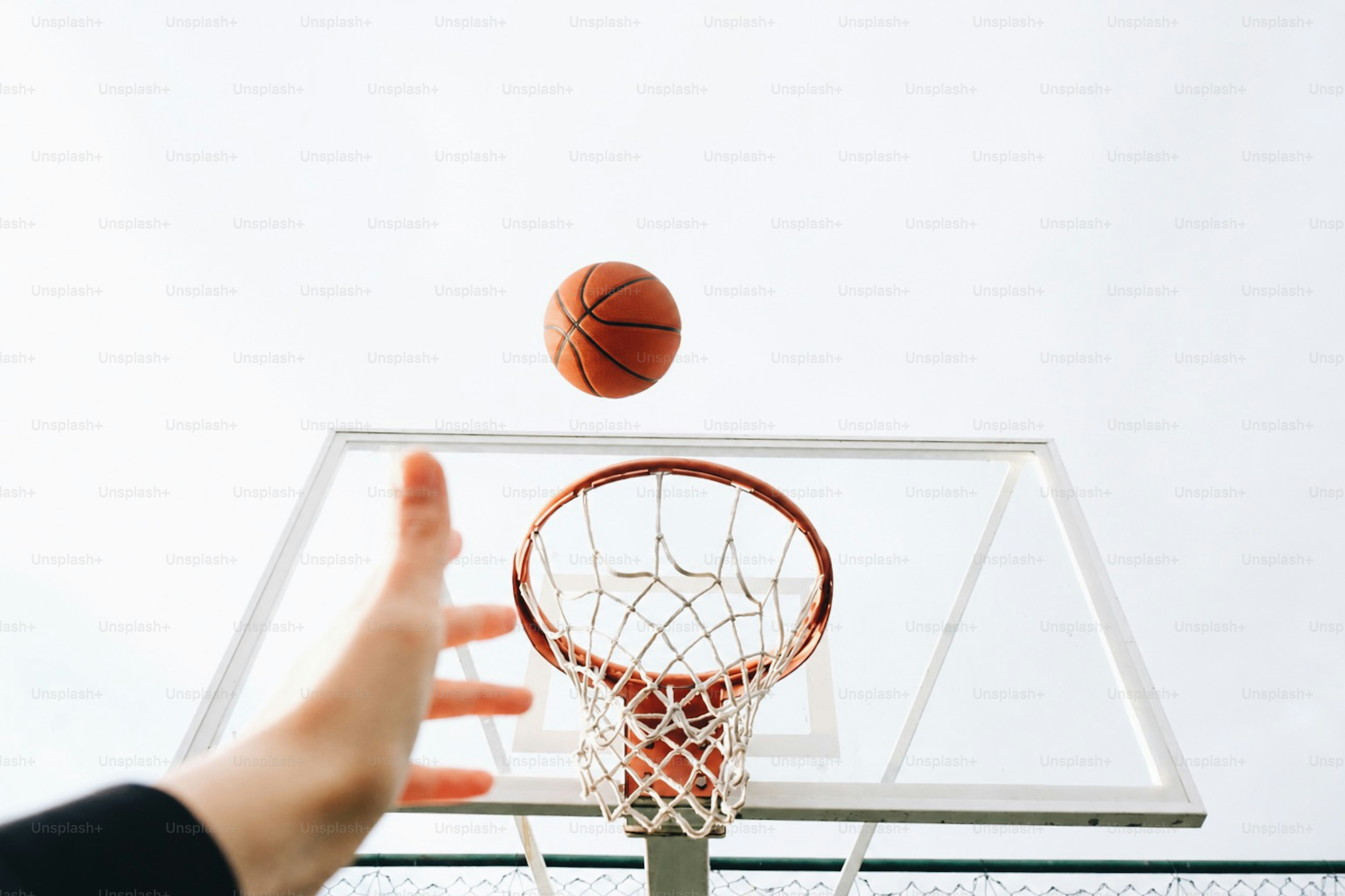 Una mano si allunga verso un pallone da basket che cade nel canestro