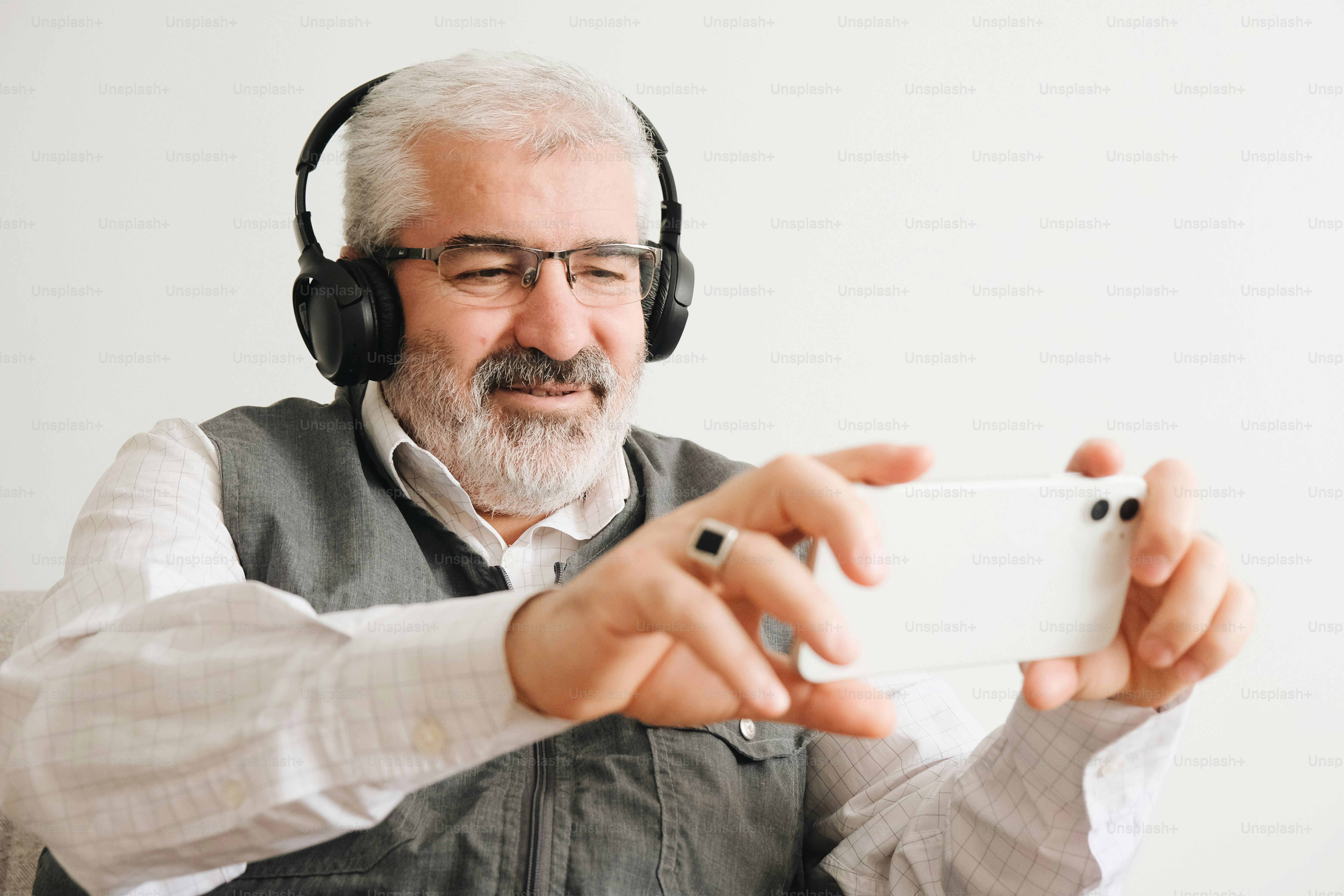 Un uomo anziano felice con le cuffie usa uno smartphone bianco