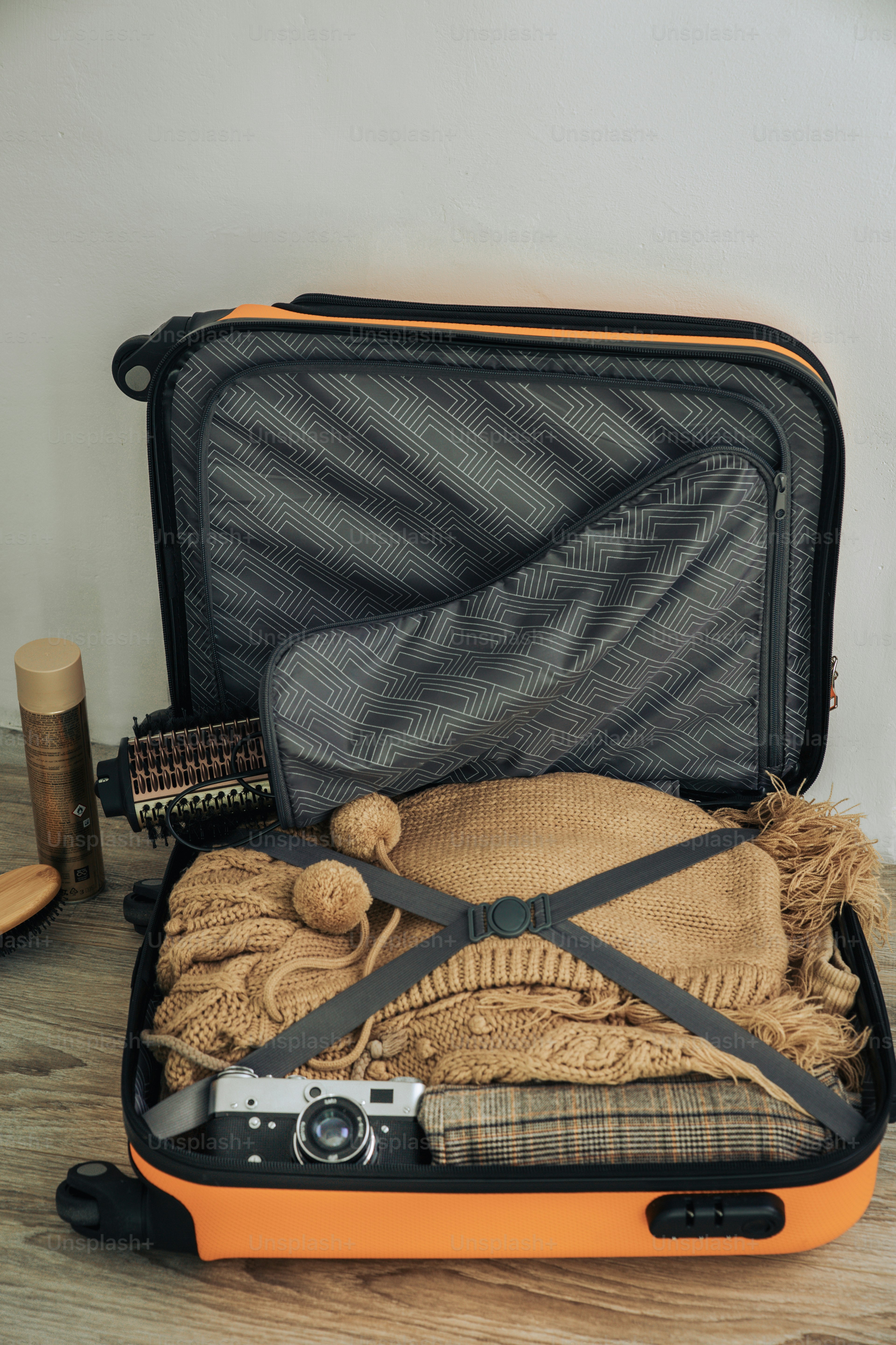 Valise orange ouverte remplie de vêtements, d’appareil photo et d’essentiels de voyage.
