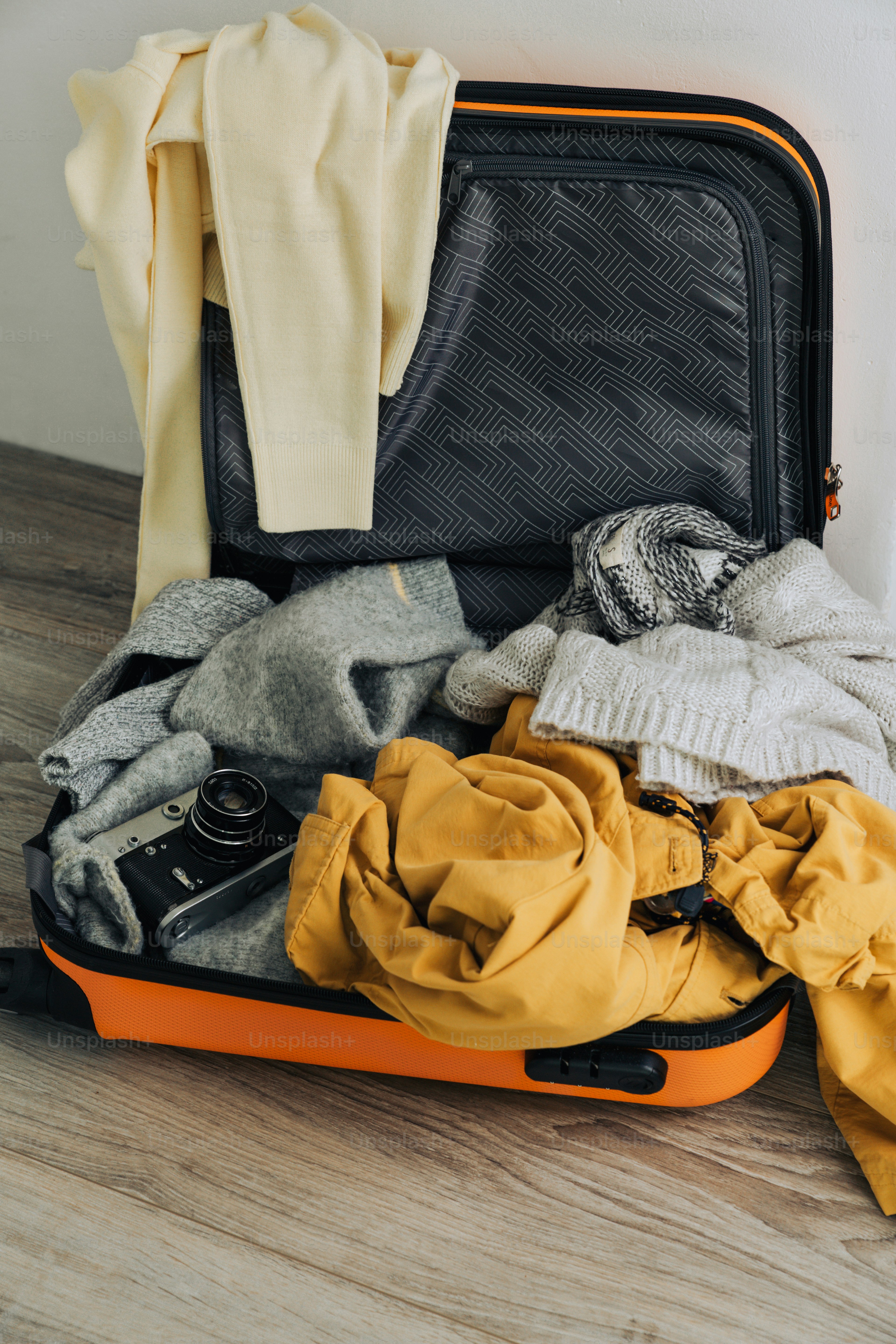 Une valise ouverte débordante de vêtements et d’un appareil photo vintage.