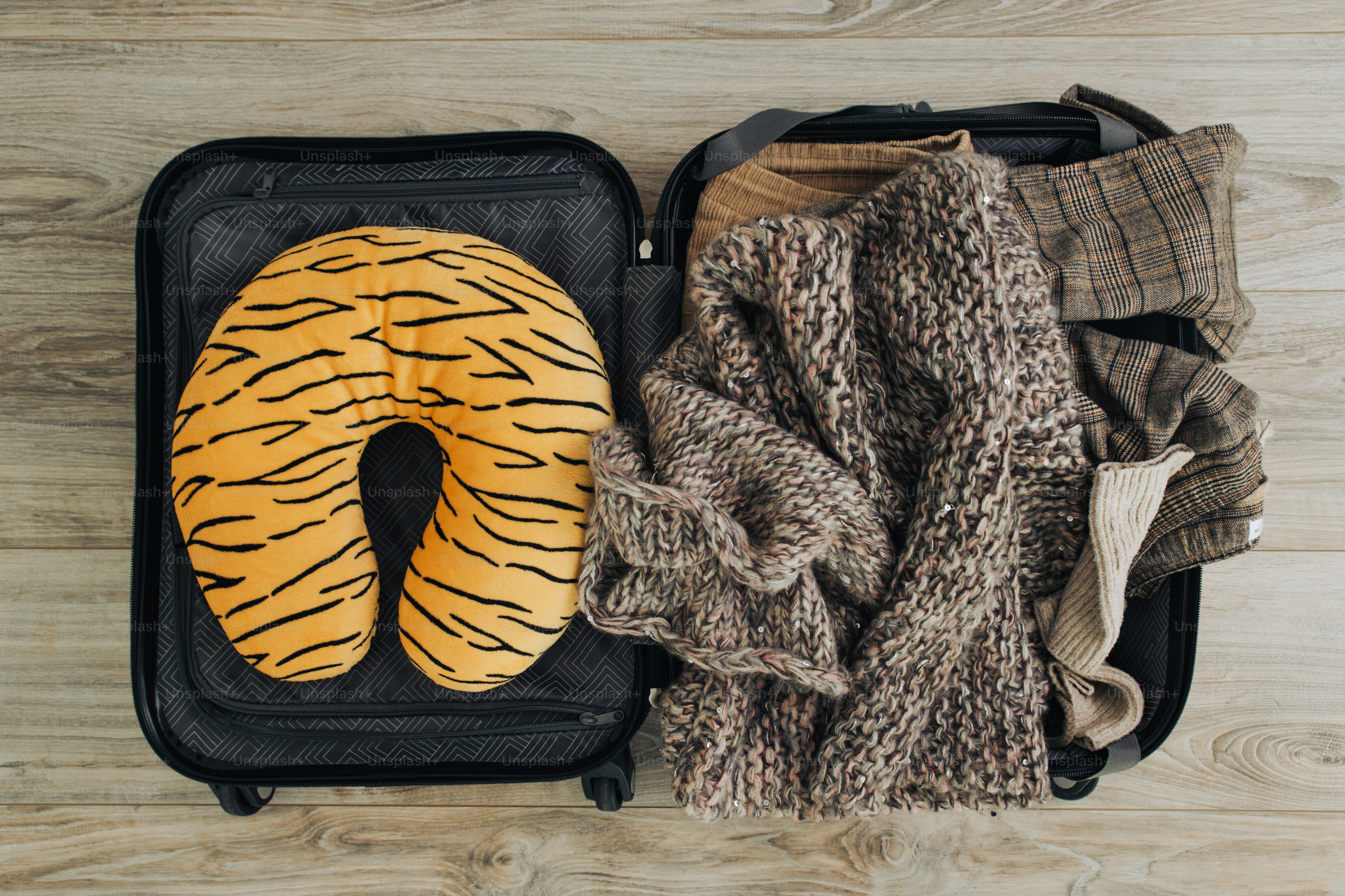 Une valise ouverte avec un coussin en forme de tigre et des vêtements.