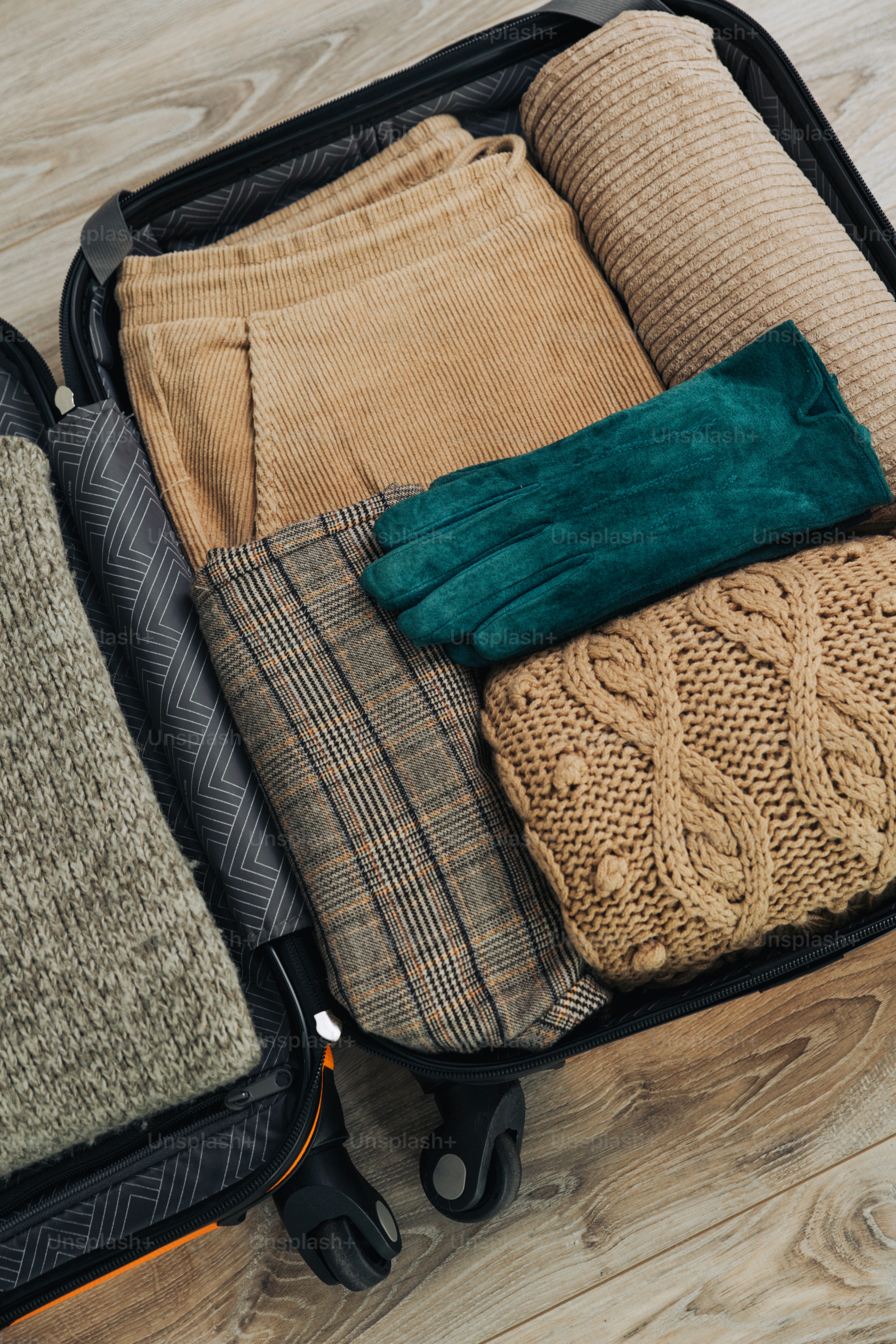 Valise de voyage remplie de vêtements chauds et de gants verts.