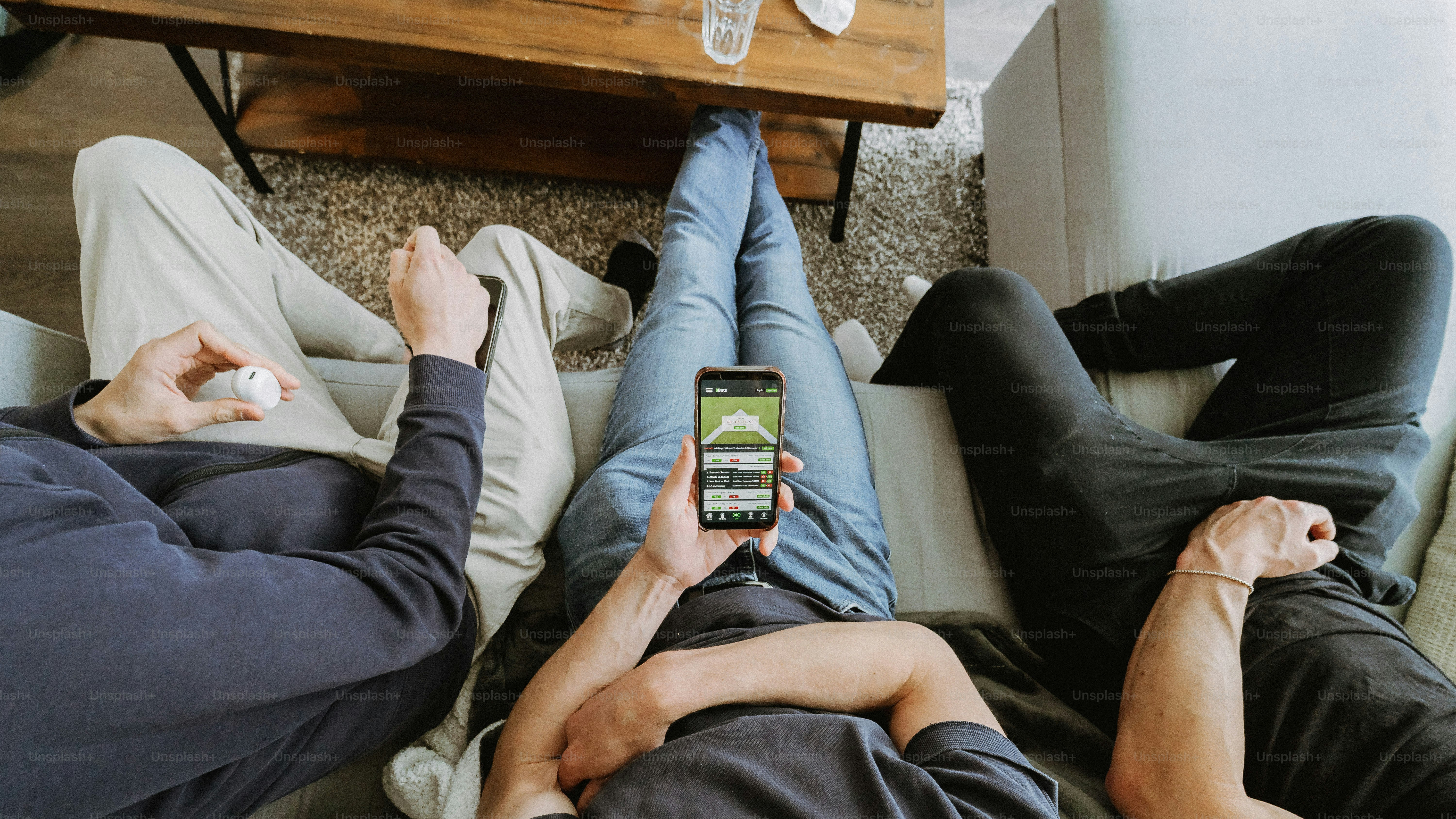 Tiga orang bersantai di sofa, satu menggunakan smartphone.