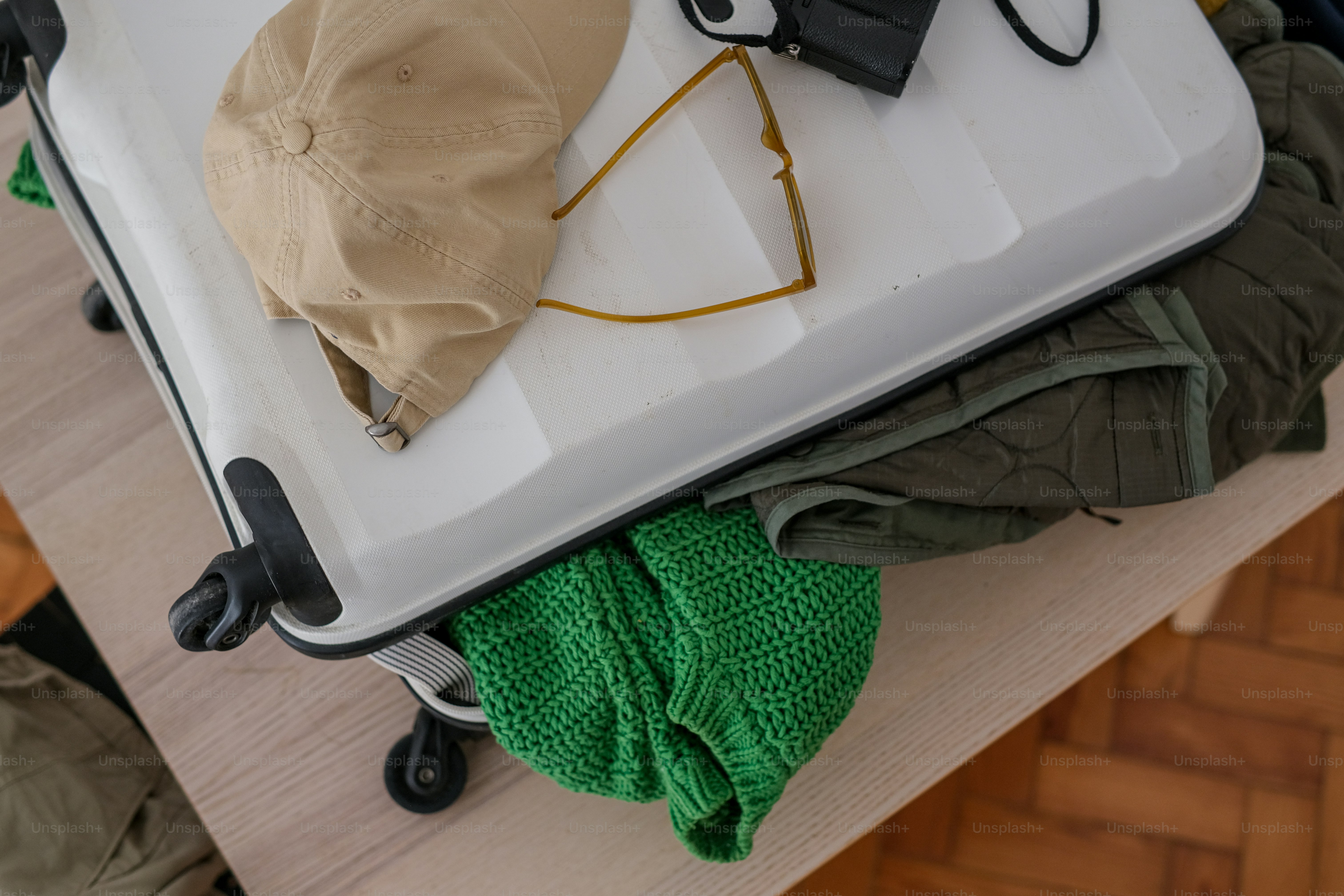 White suitcase, beige cap, sunglasses, and green clothes.
