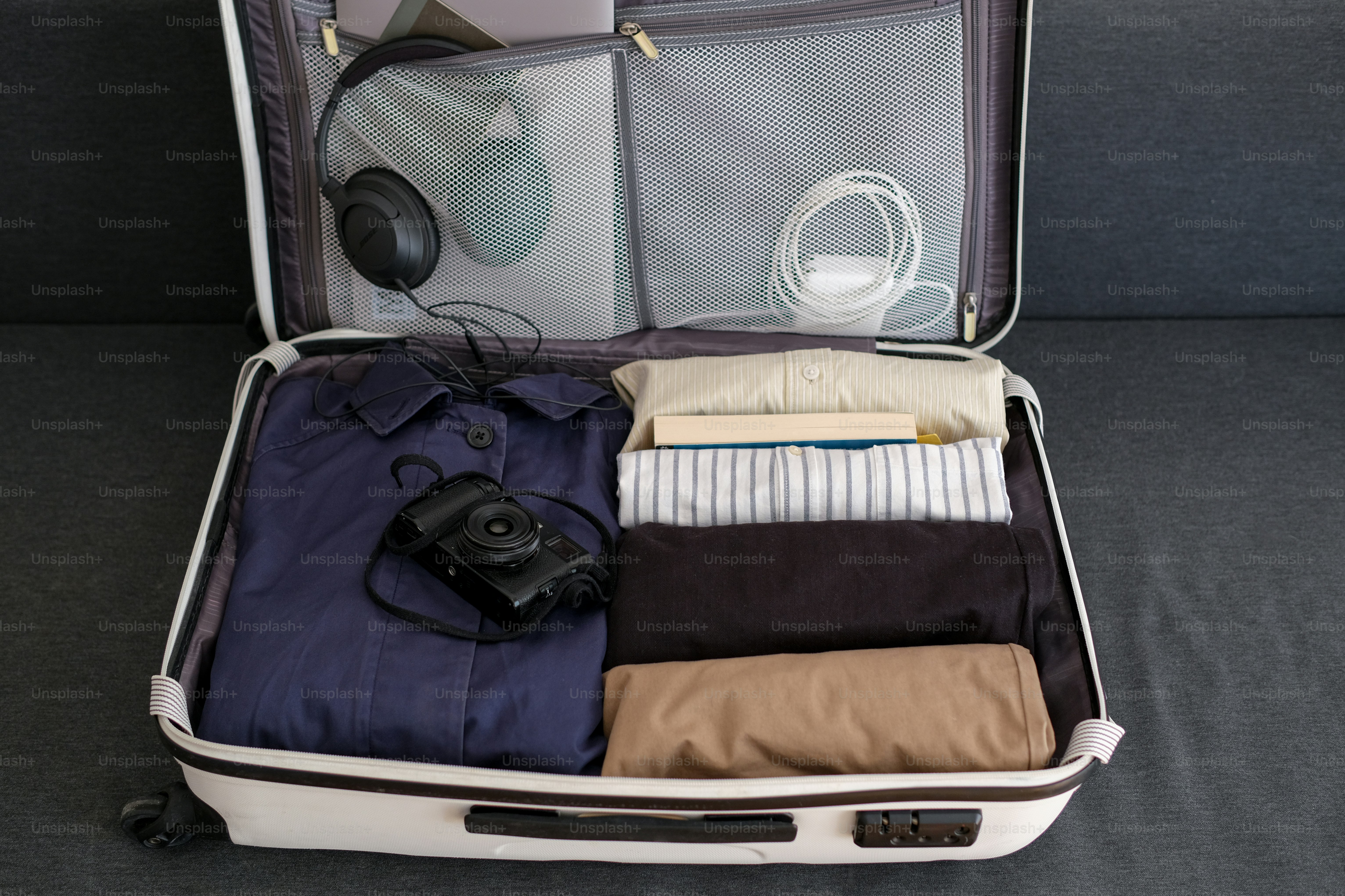 An open suitcase packed with clothes, camera, and headphones.