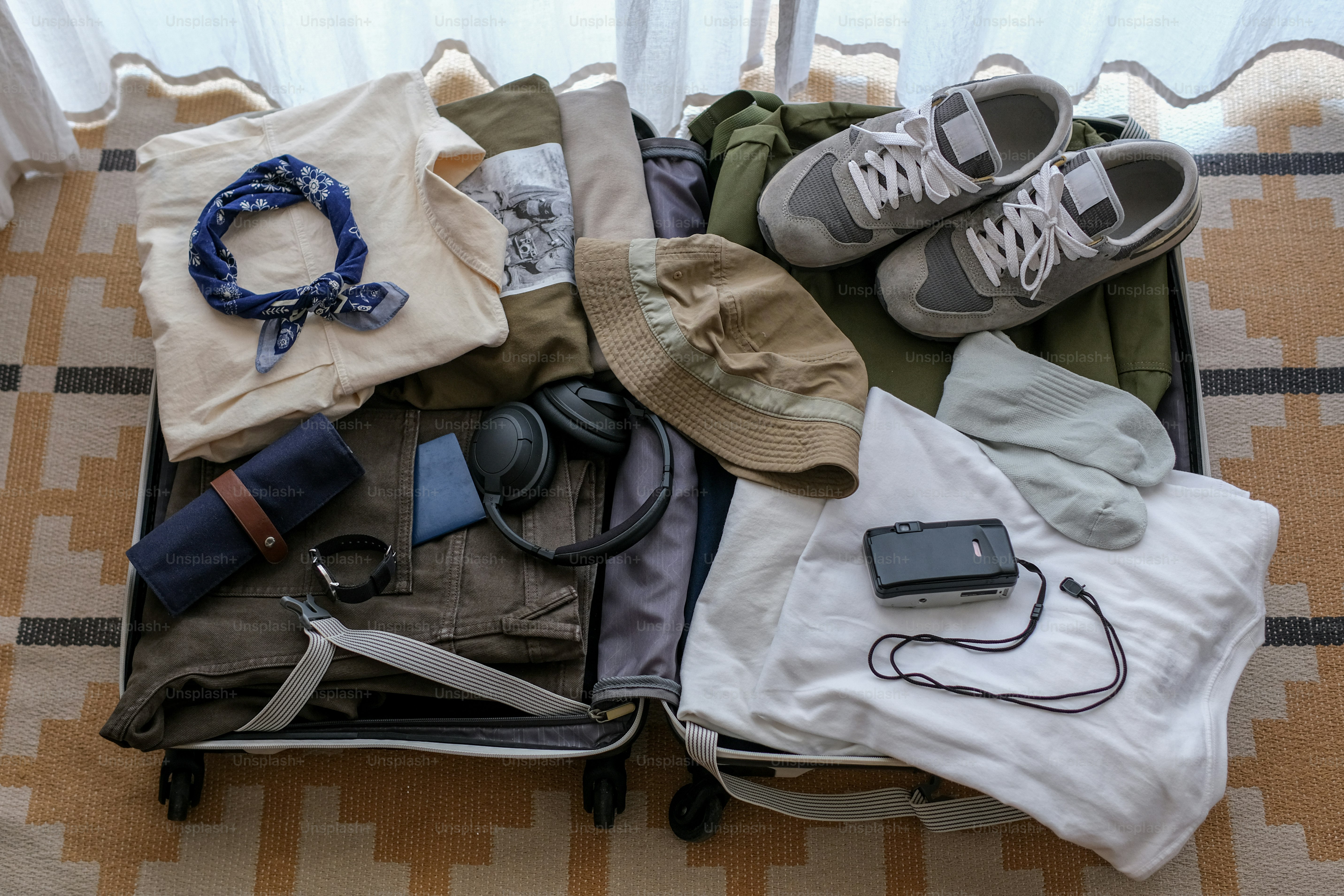 An open suitcase packed with clothes, shoes, and travel accessories.
