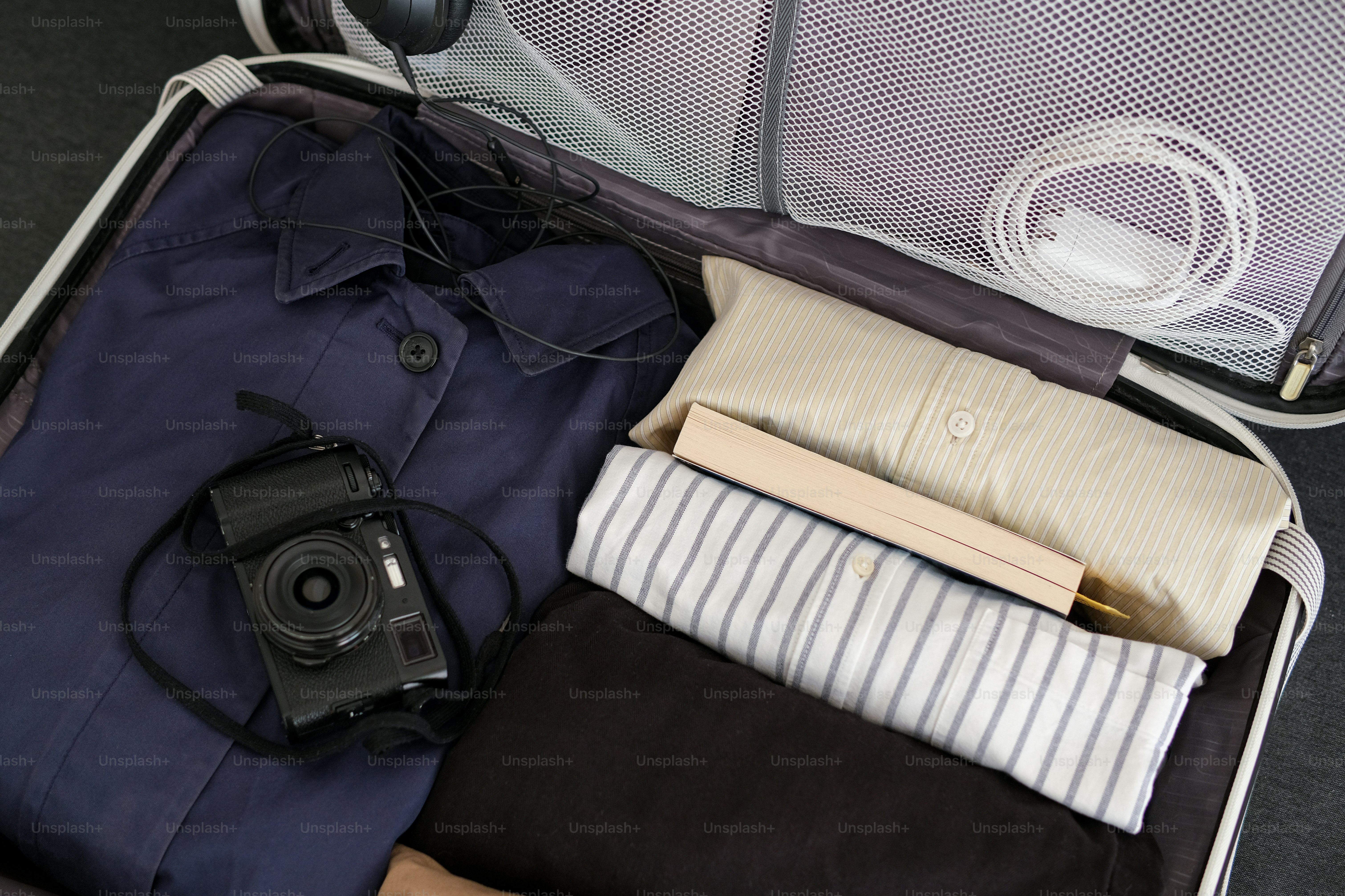 An open suitcase packed with clothes and a camera.