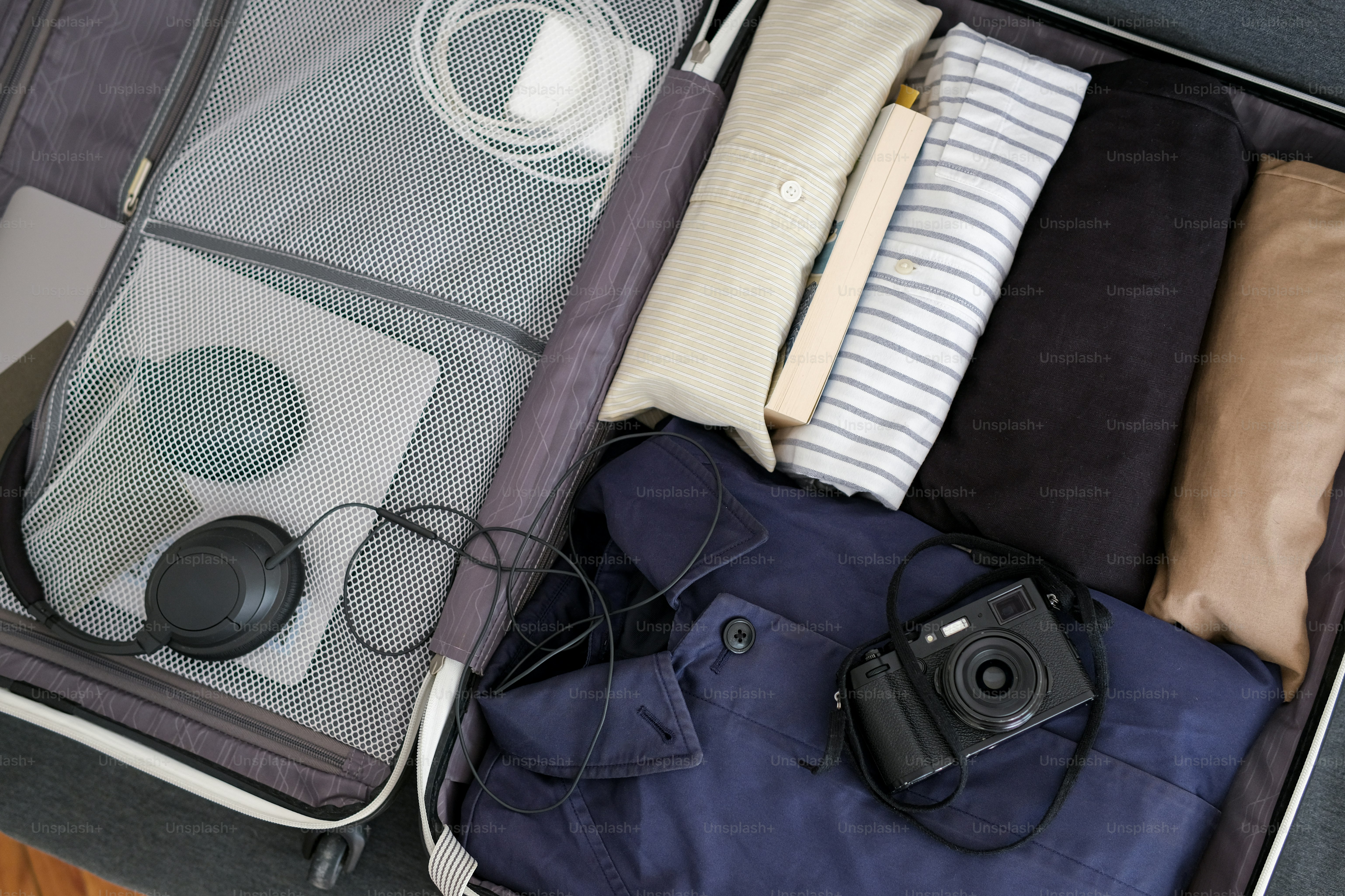 Travel suitcase packed with clothes, camera, and headphones.