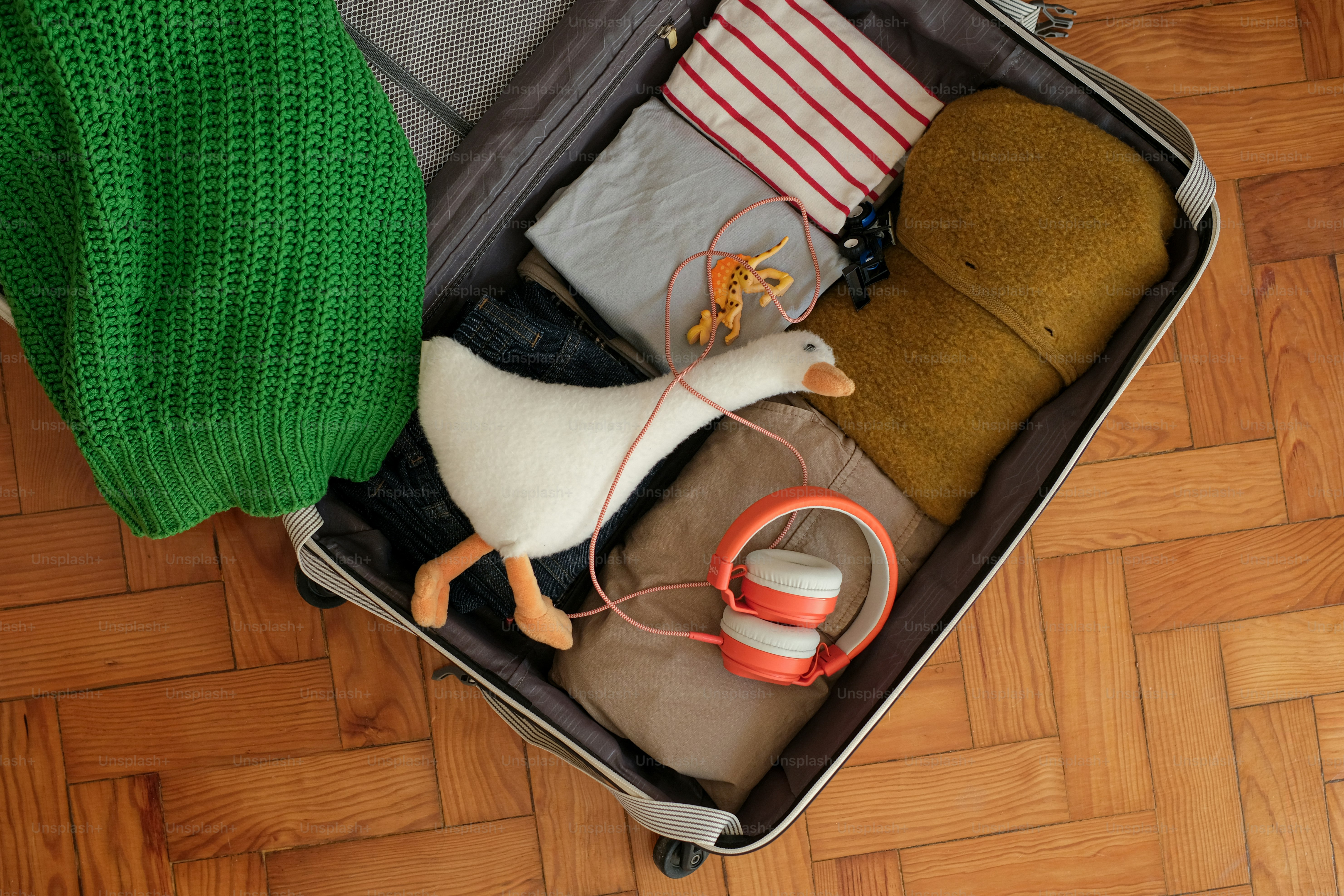 Open suitcase with clothes, a toy goose, and headphones.