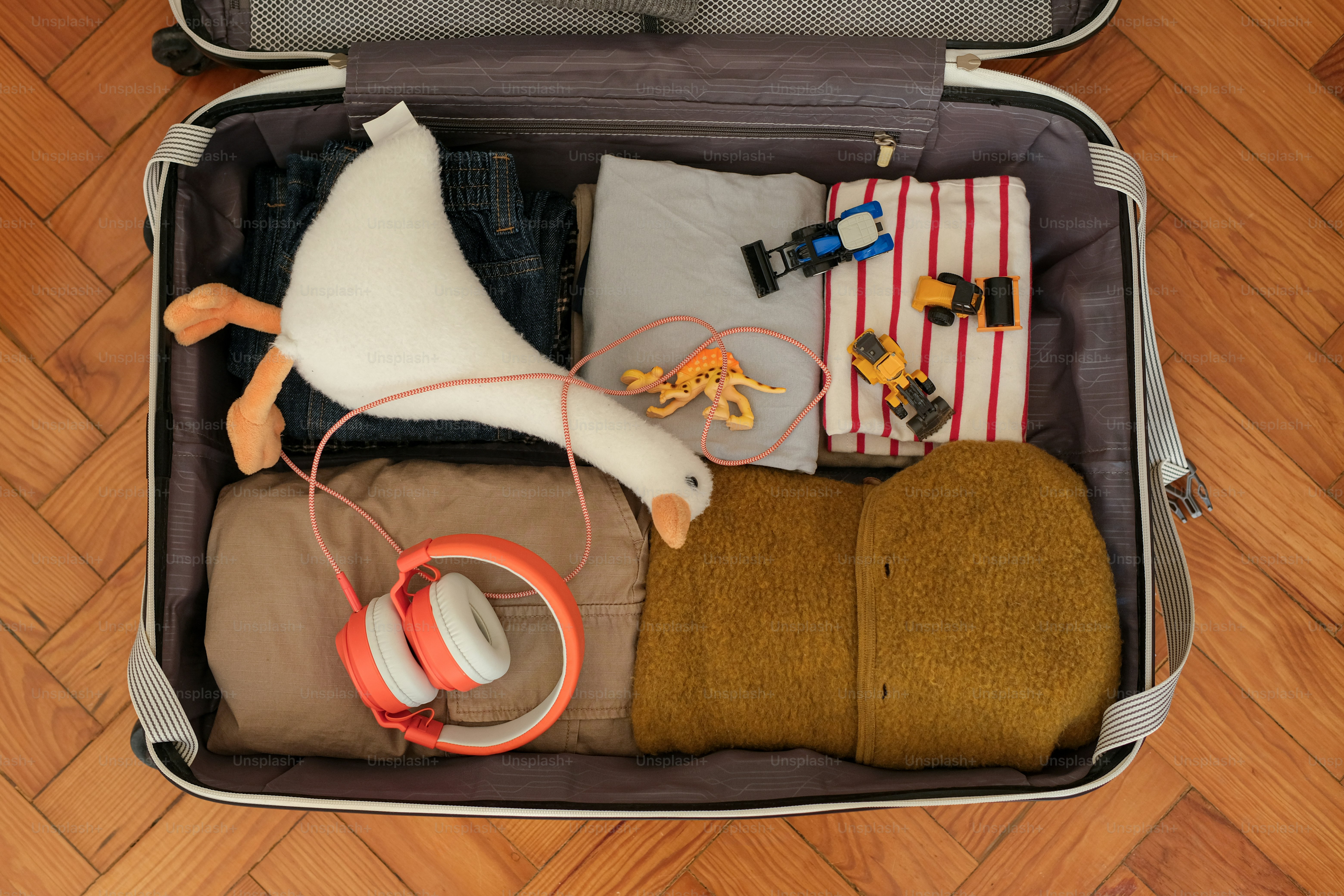 Open suitcase packed with clothes, toy goose, and headphones.