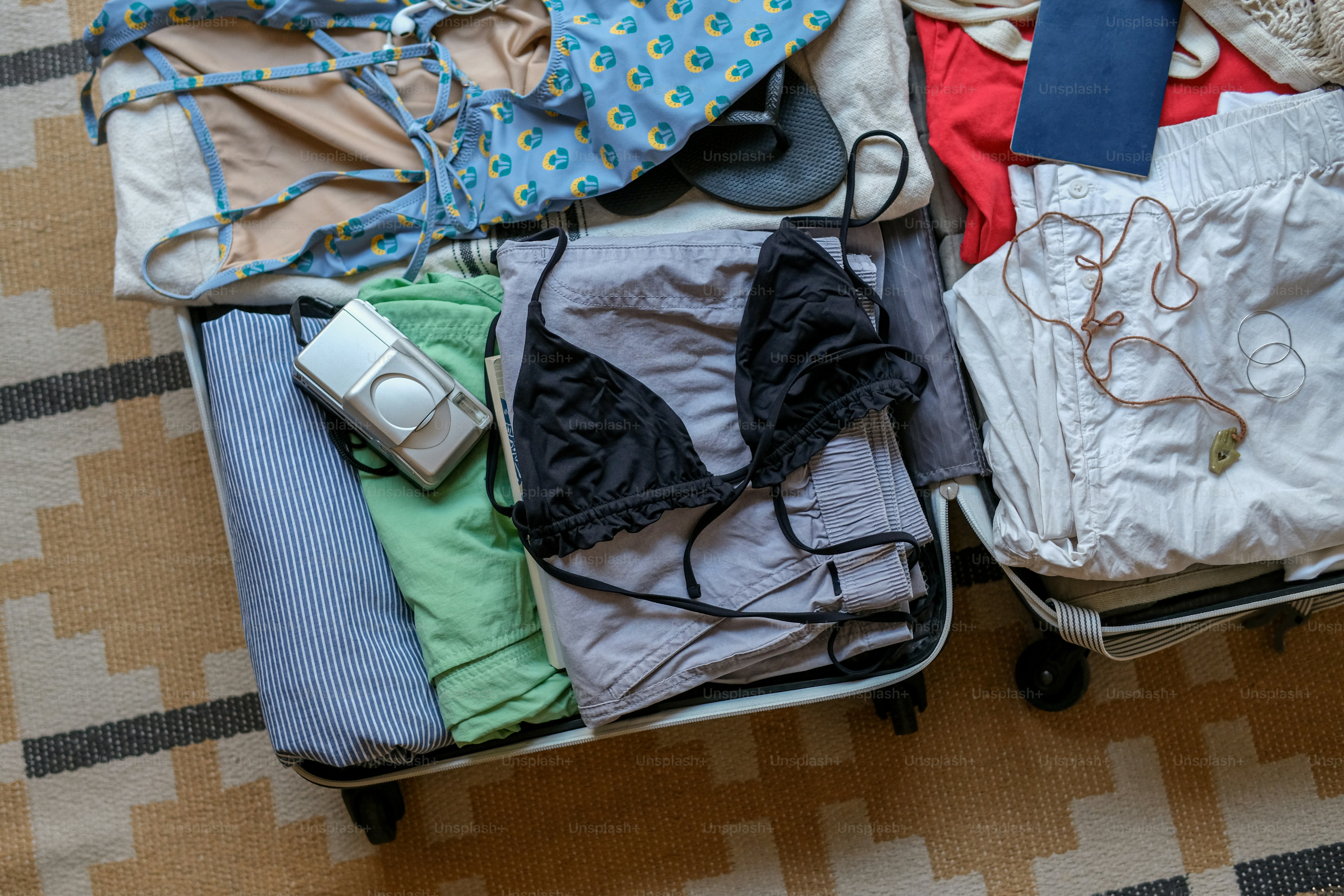 Two open suitcases packed with various clothes and a camera.