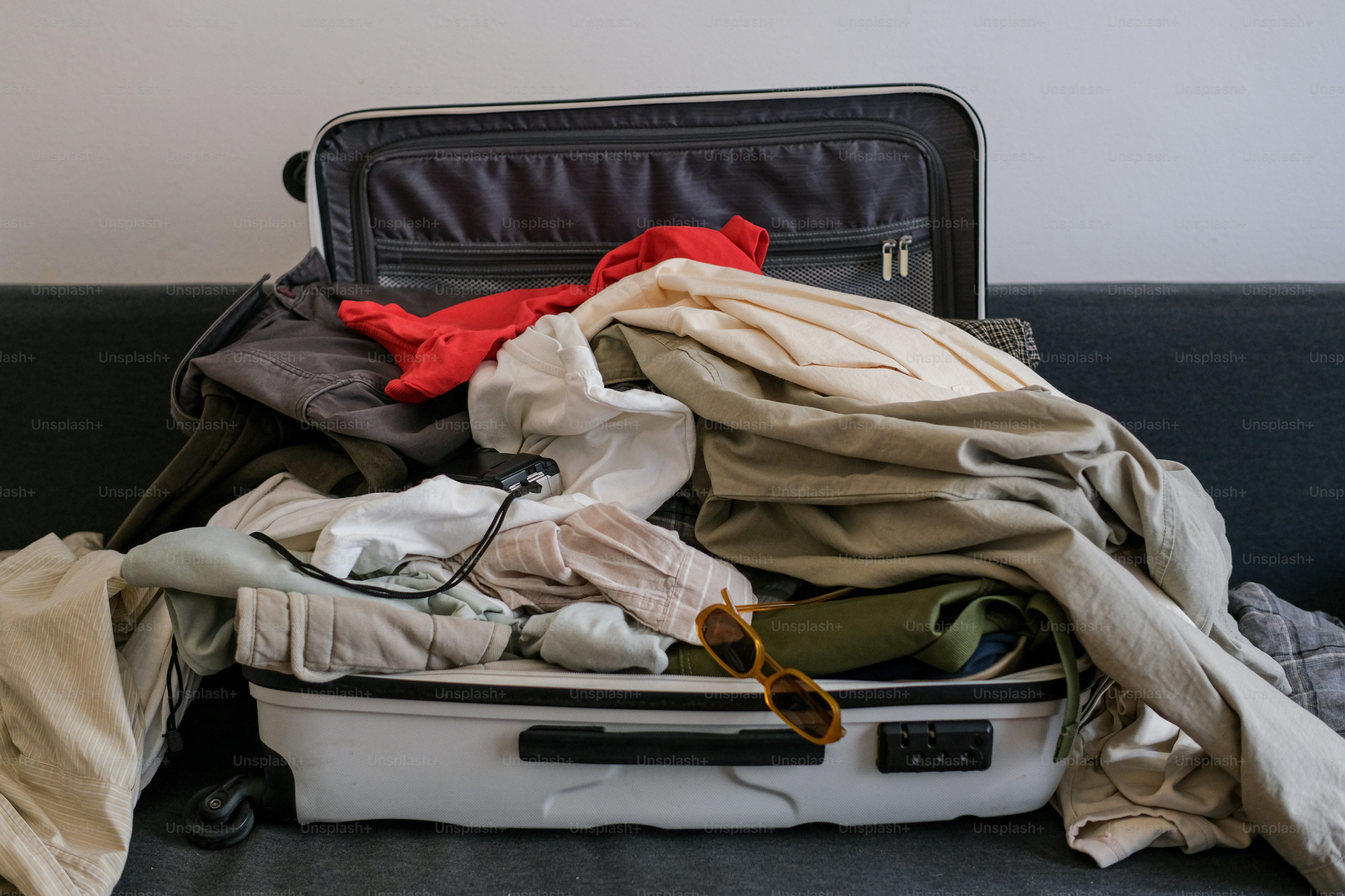 An open suitcase filled with clothes and sunglasses.