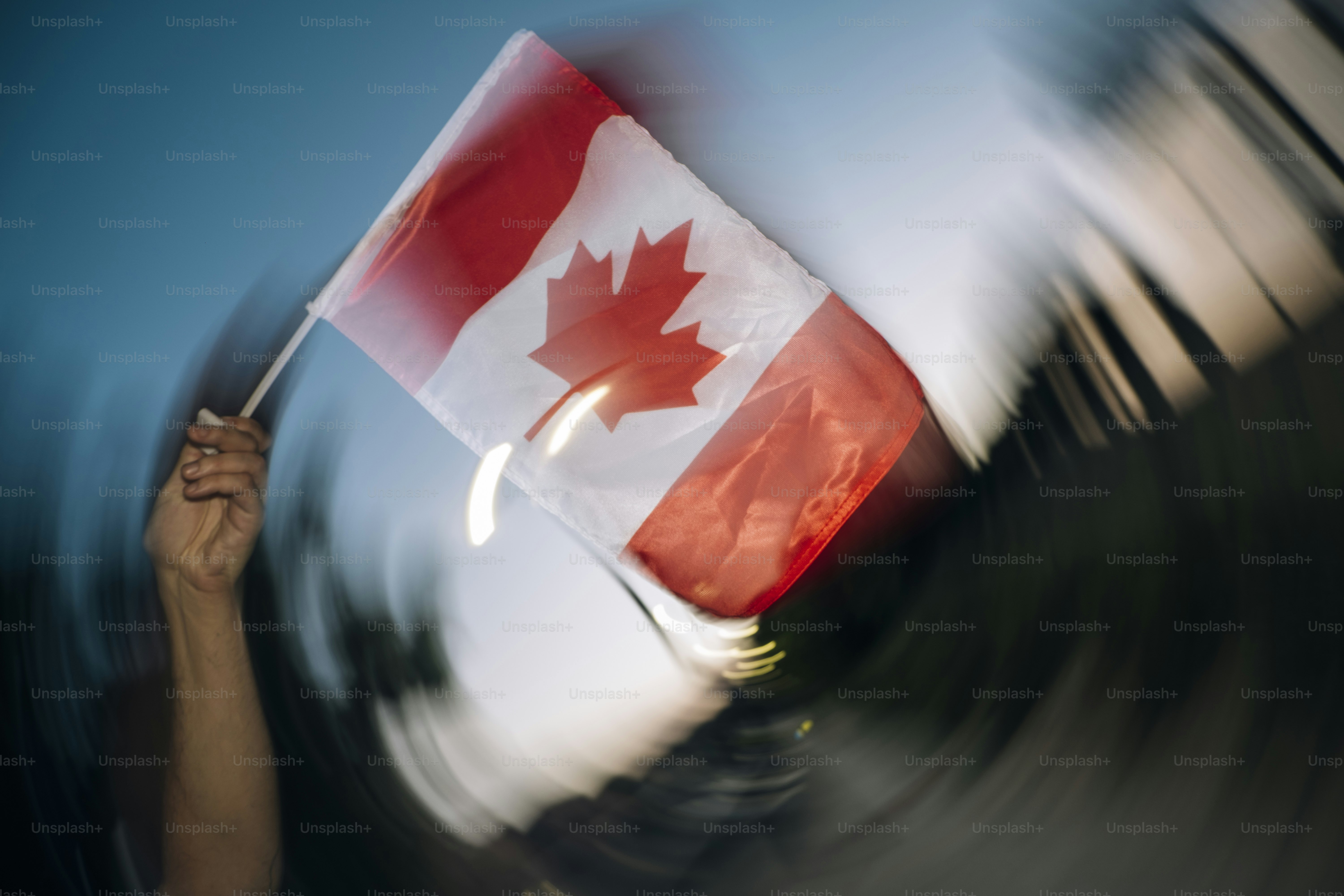 A hand waves a canadian flag against a blurred background.