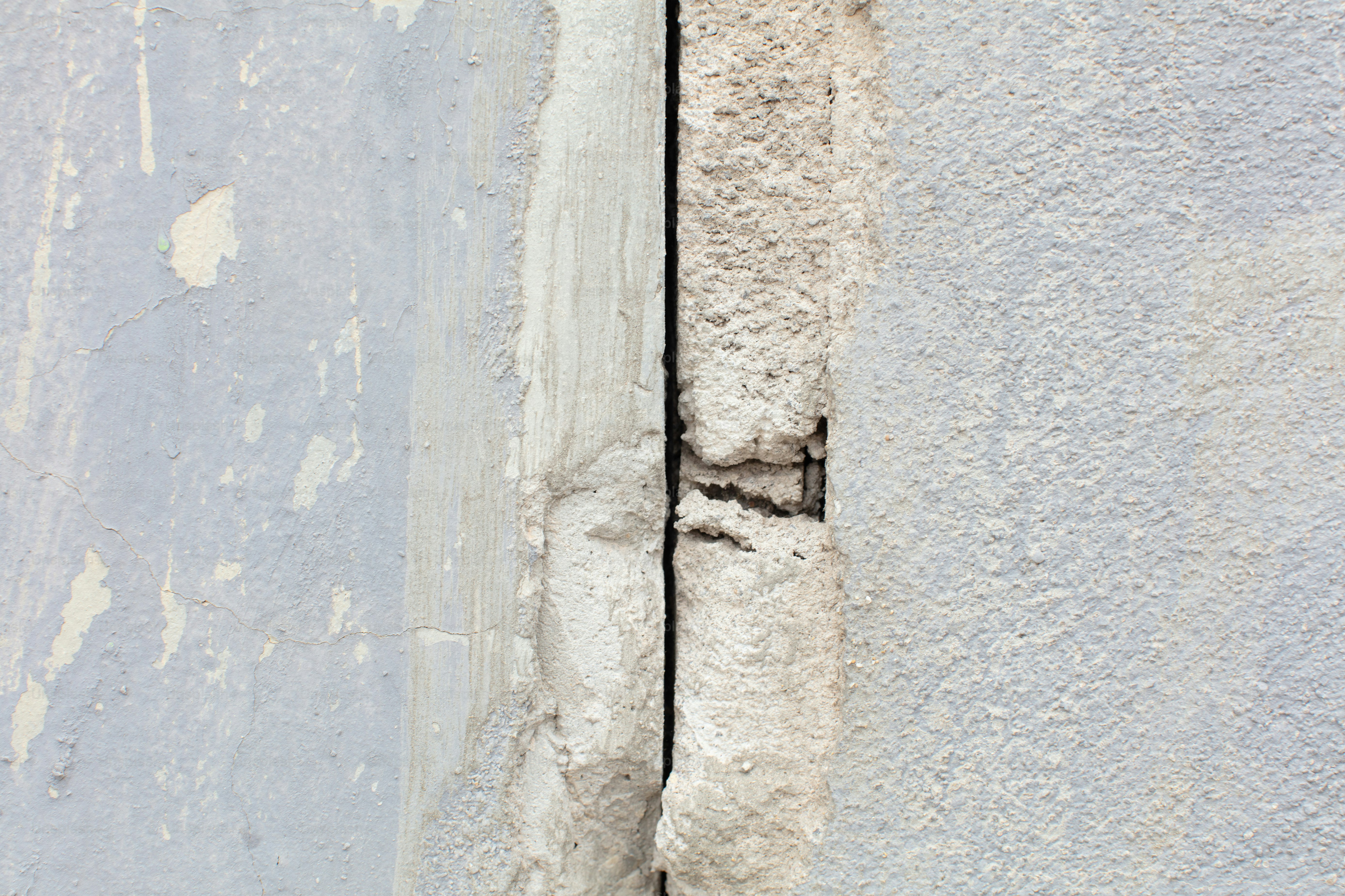 Concrete wall surface with a deep crack, flaking paint, and rough texture