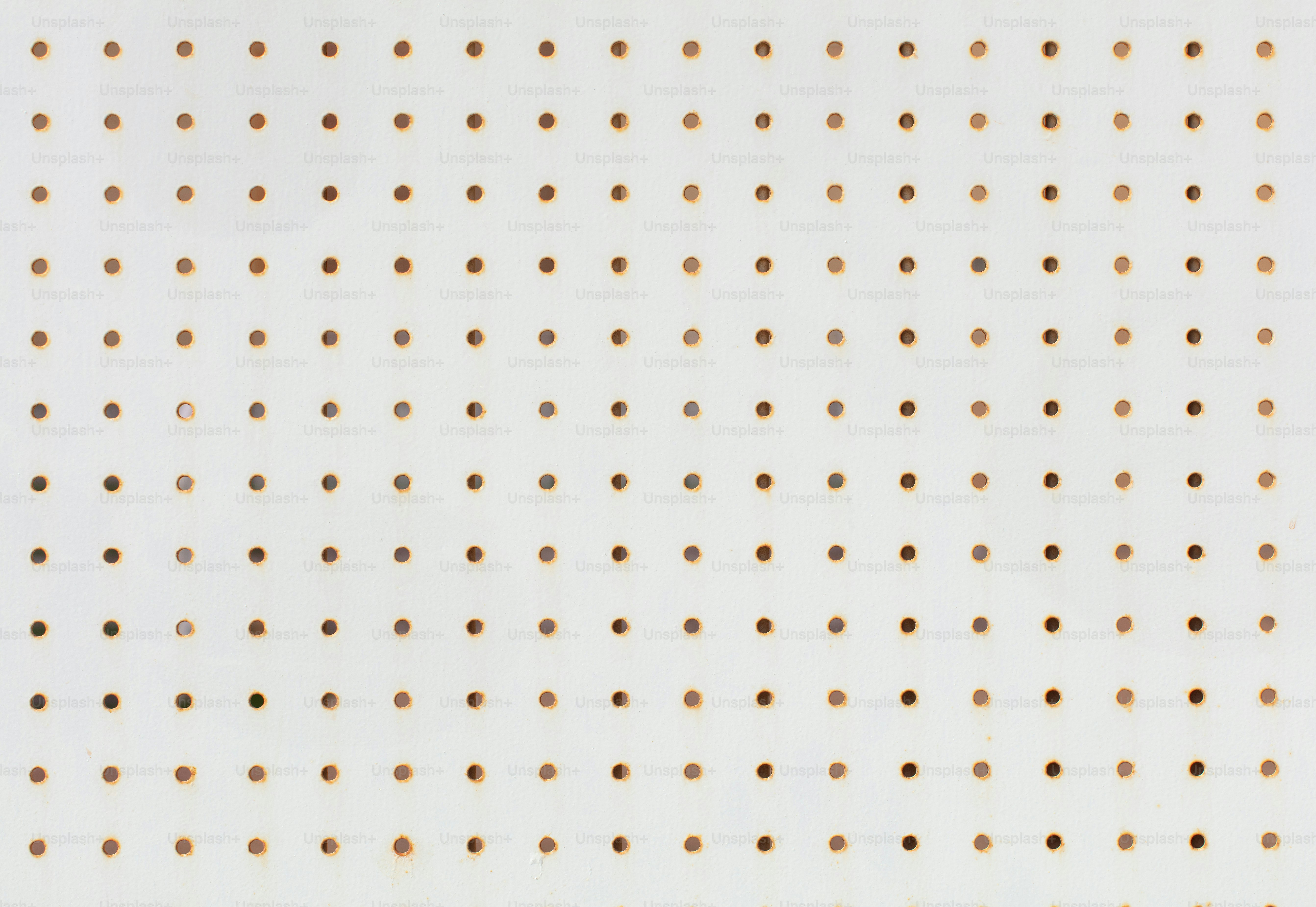 Surface de panneau perforé blanc avec des trous bruns espacés uniformément.