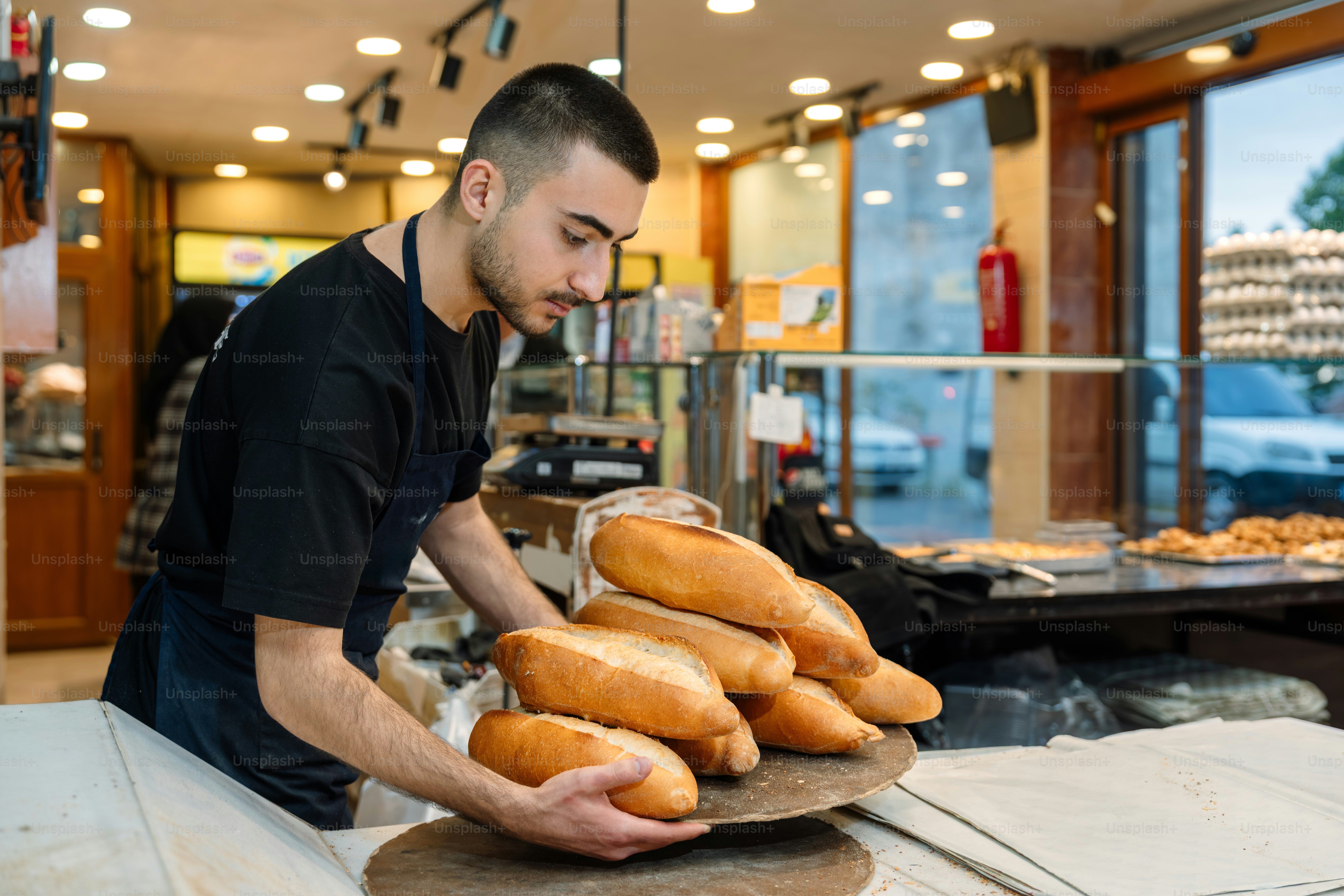 A young man arranging freshly baked bread in a bakery.