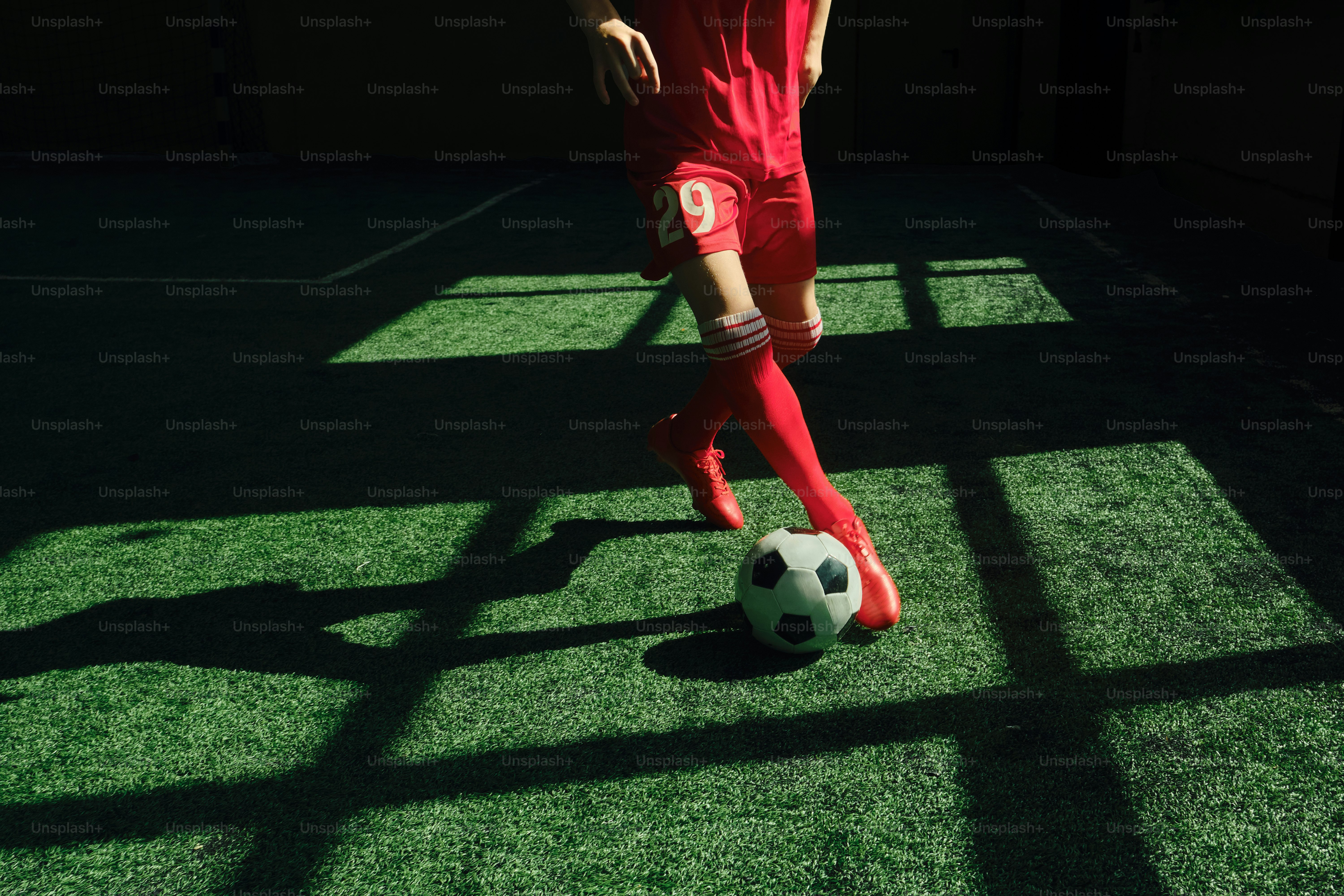 A soccer ball on a green field with red cleats. photo – Football Image ...