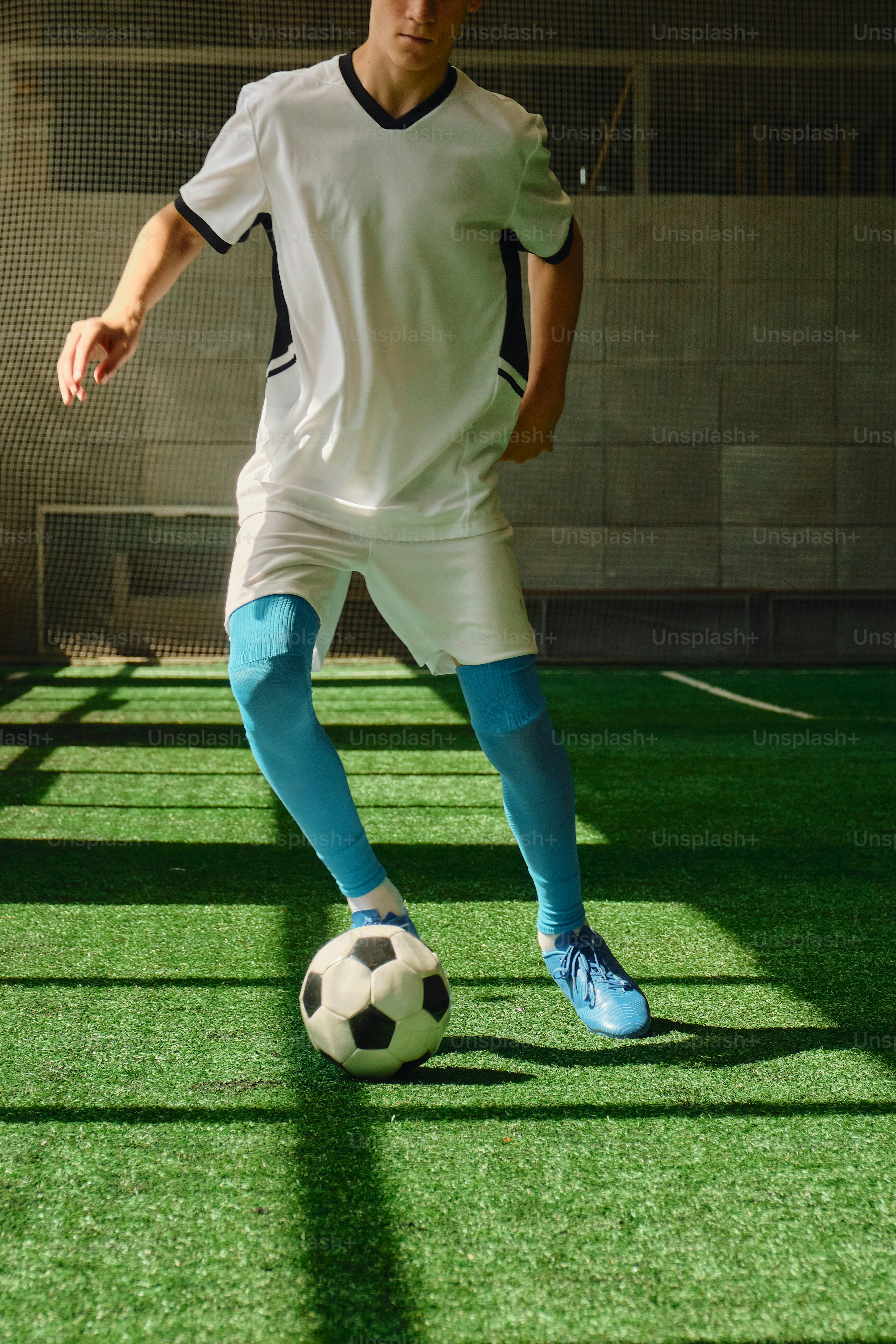 Male soccer player dribbles ball on green artificial turf.