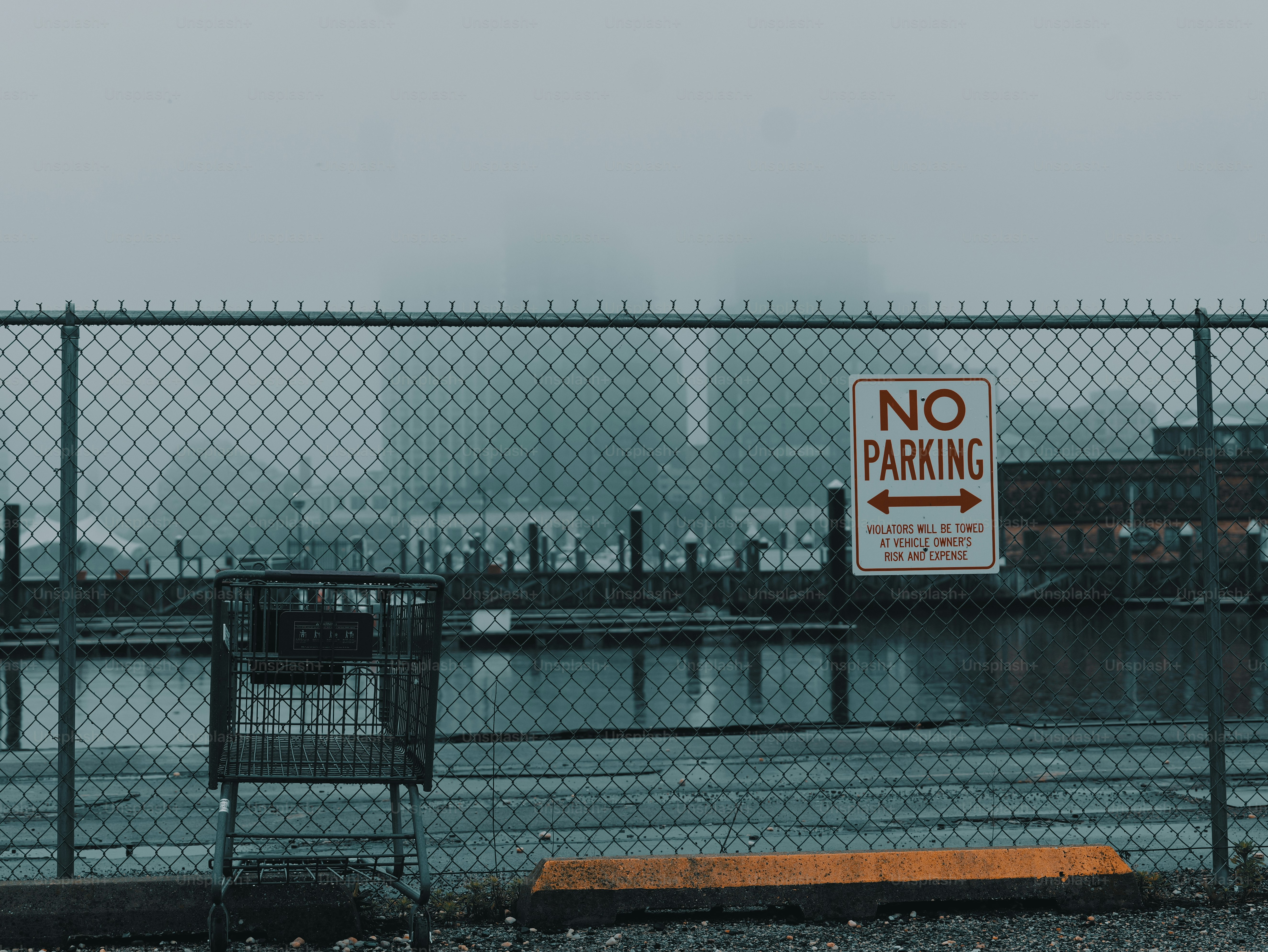 Foggy industrial scene with "no parking" sign and fence.