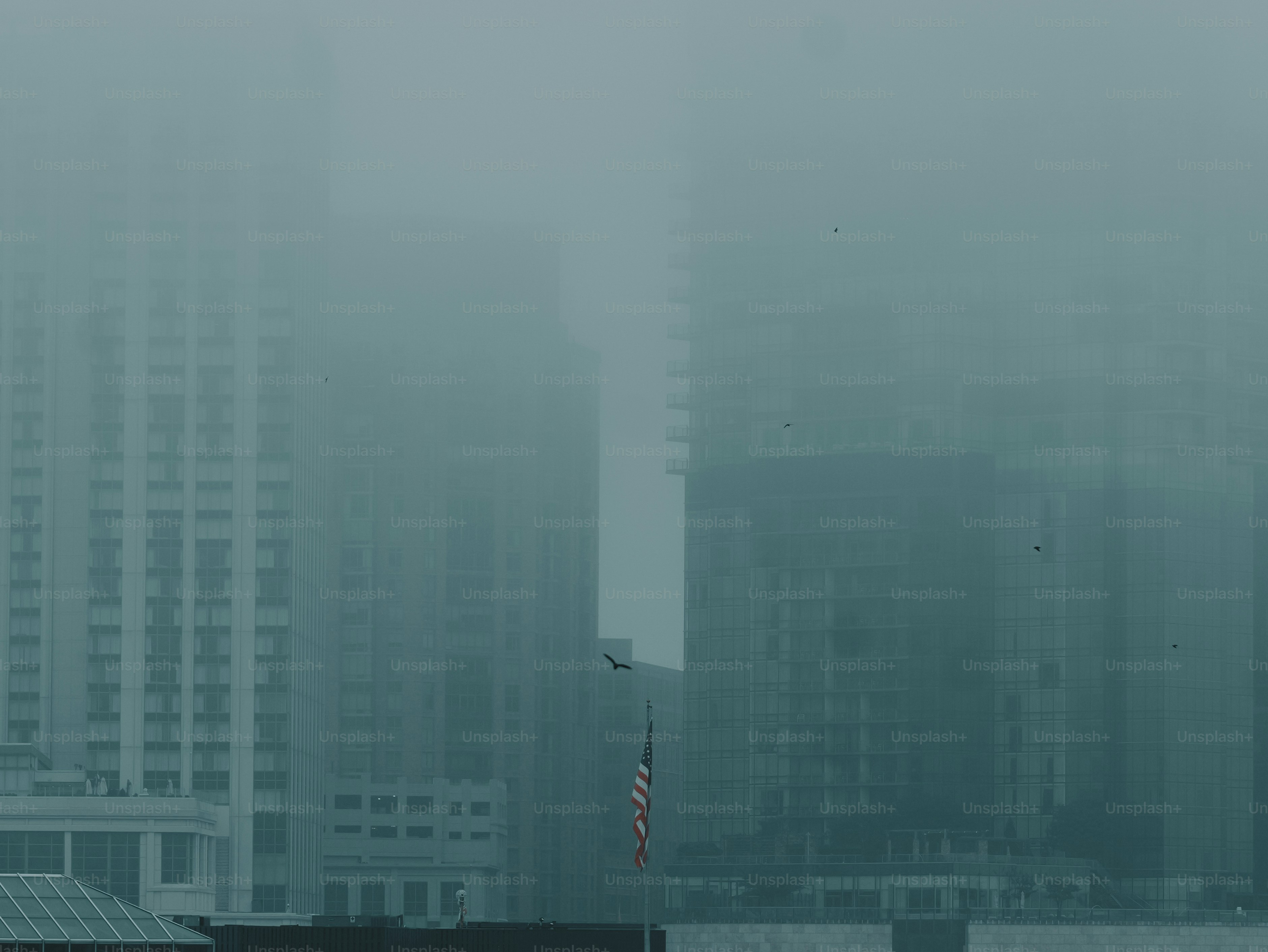Tall buildings shrouded in dense fog with a flag.