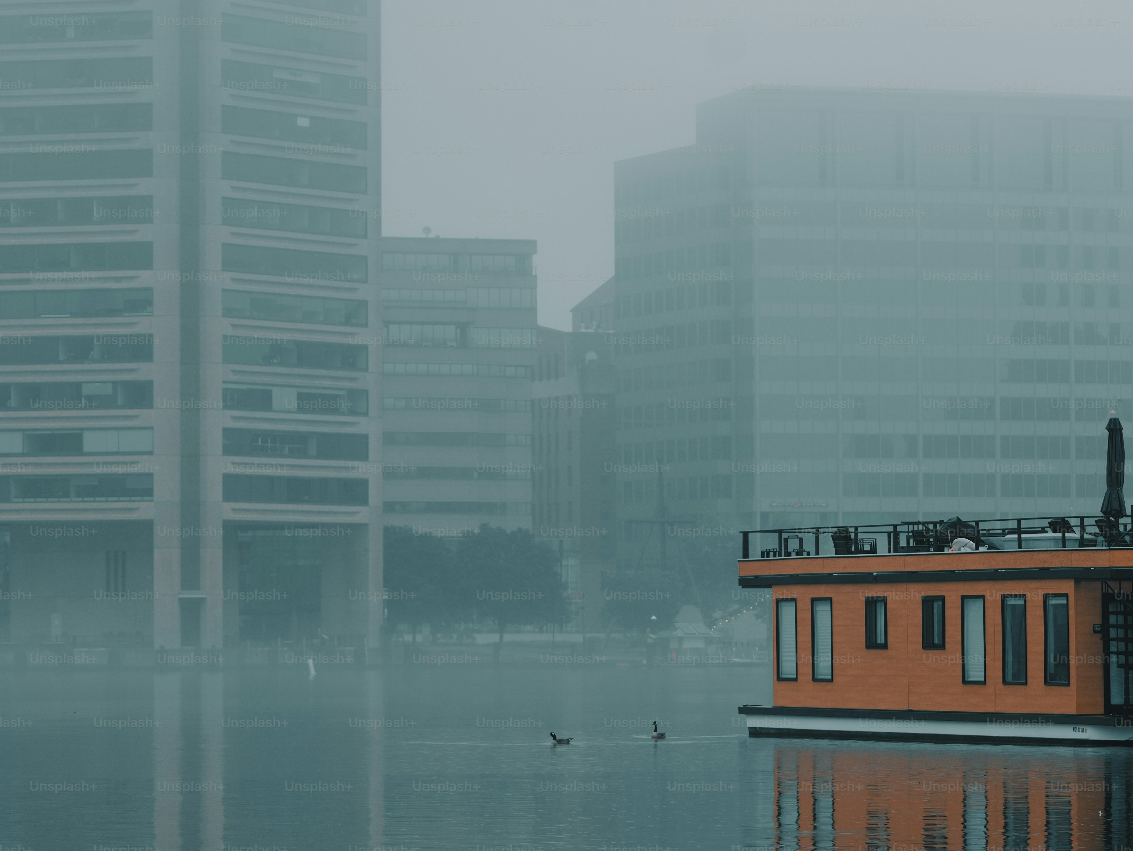 Orange houseboat and city buildings in dense fog with ducks.