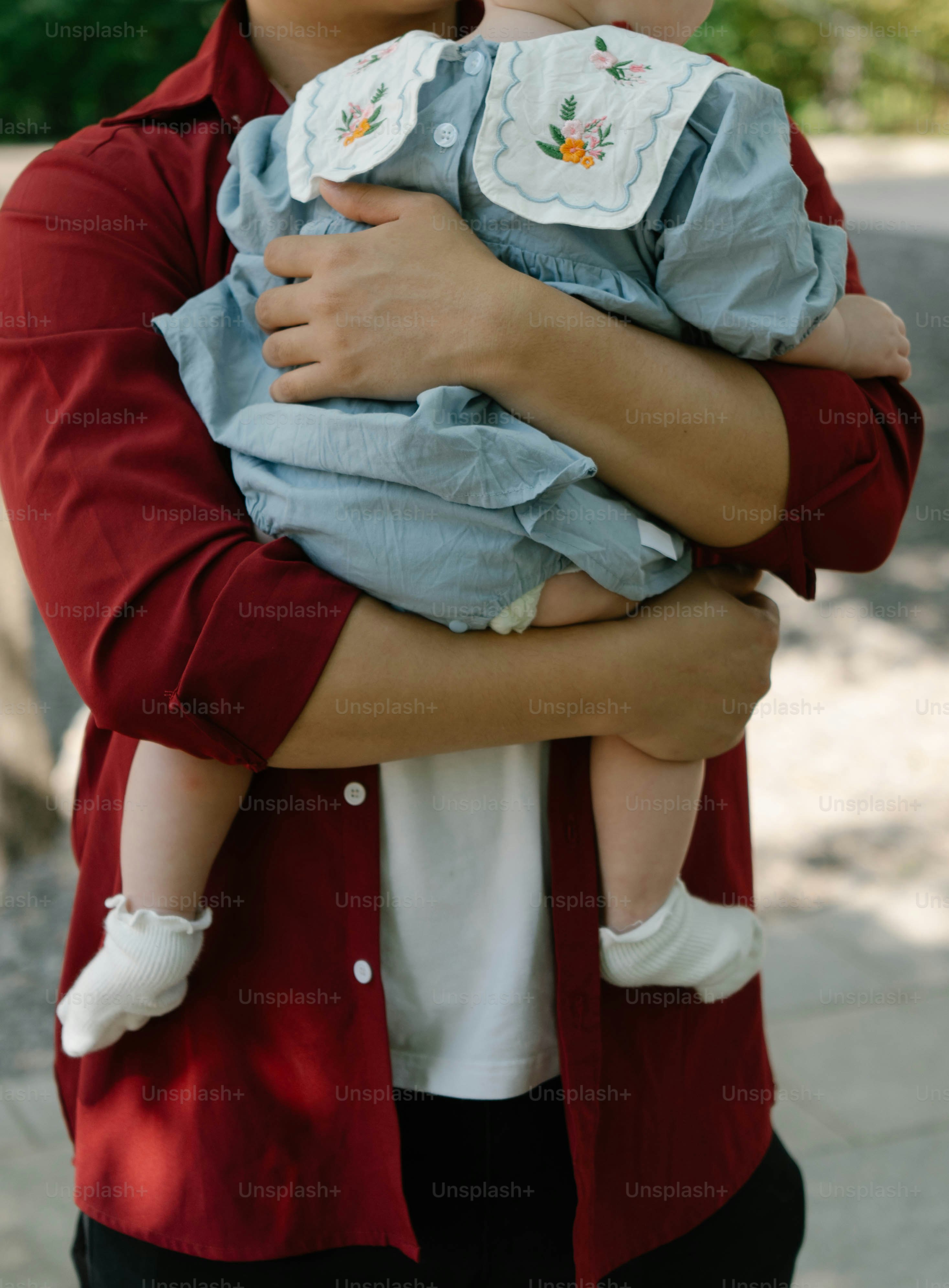 Seseorang menggendong bayi dengan gaun biru.