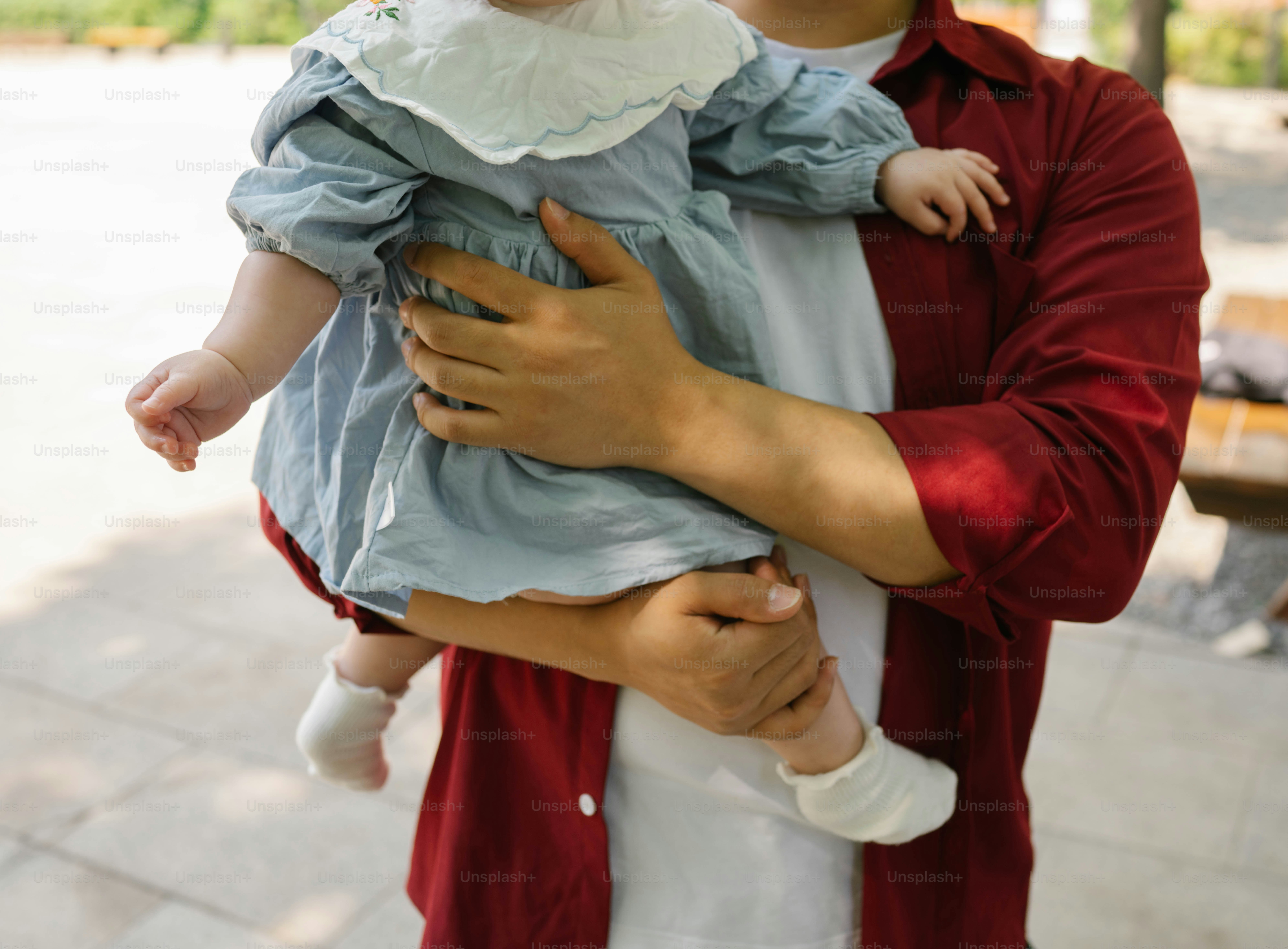 Seseorang menggendong bayi yang mengenakan gaun biru di luar ruangan.
