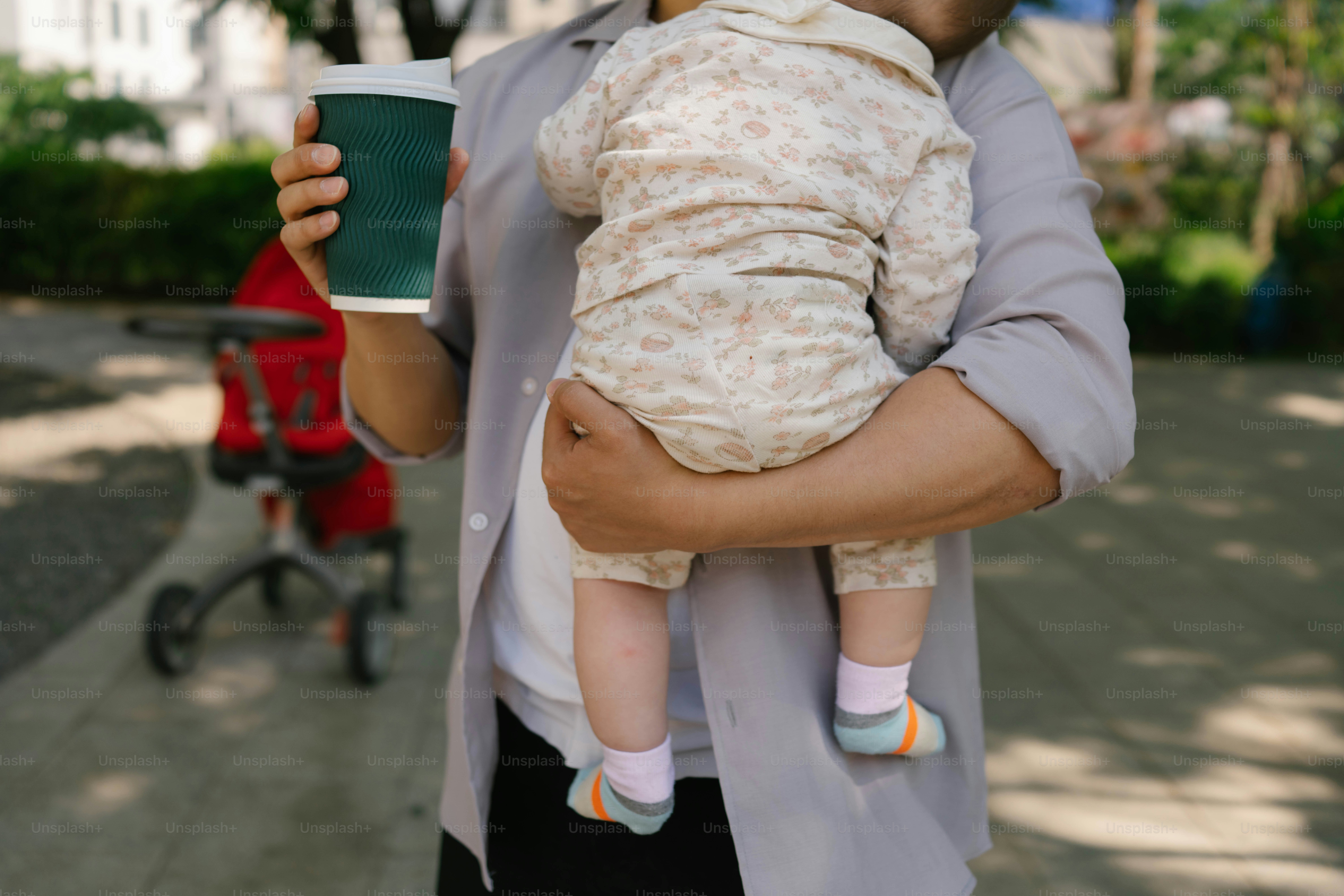 Orang yang menggendong bayi dan cangkir kopi di luar ruangan.