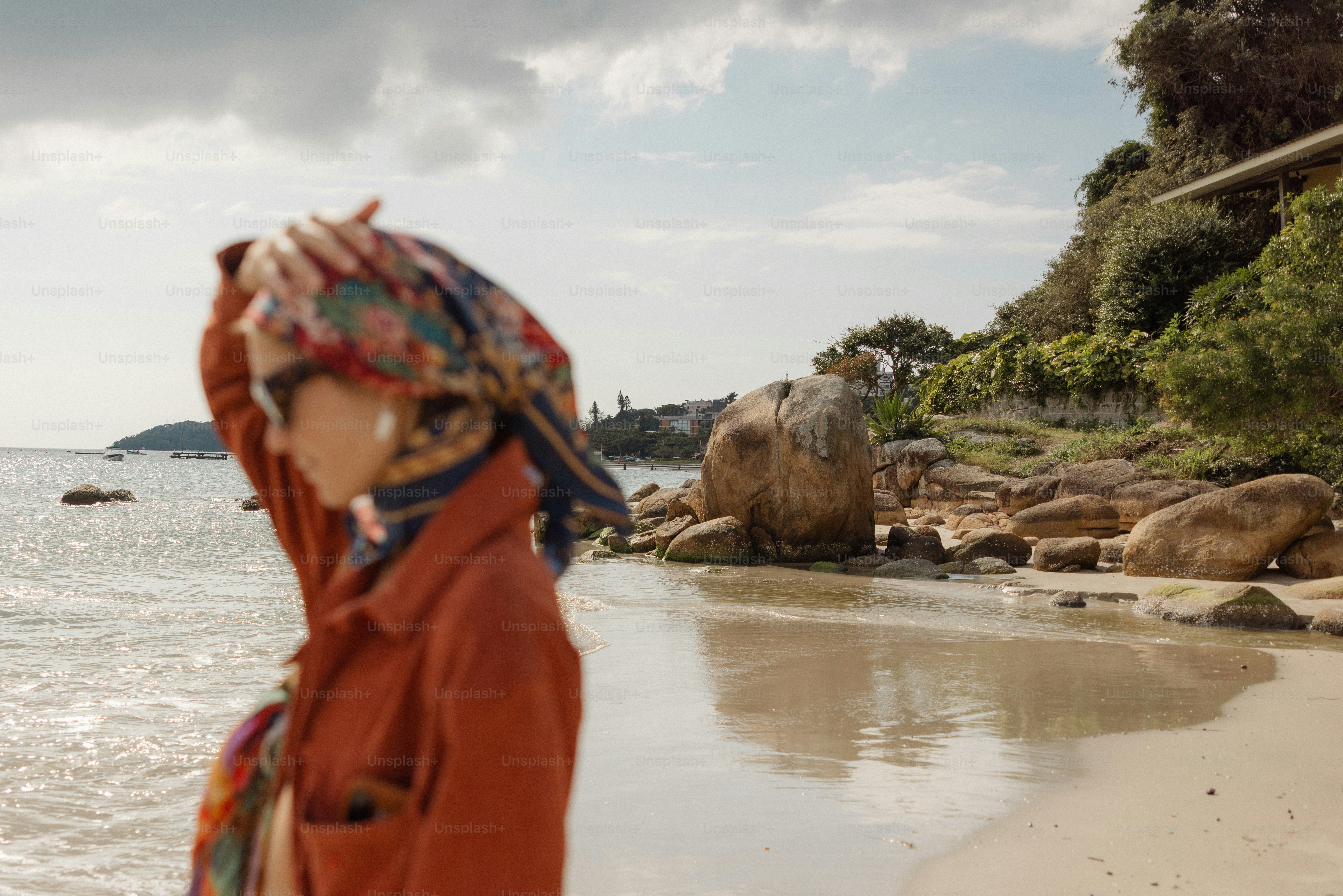 A person in a headscarf stands on a rocky beach.