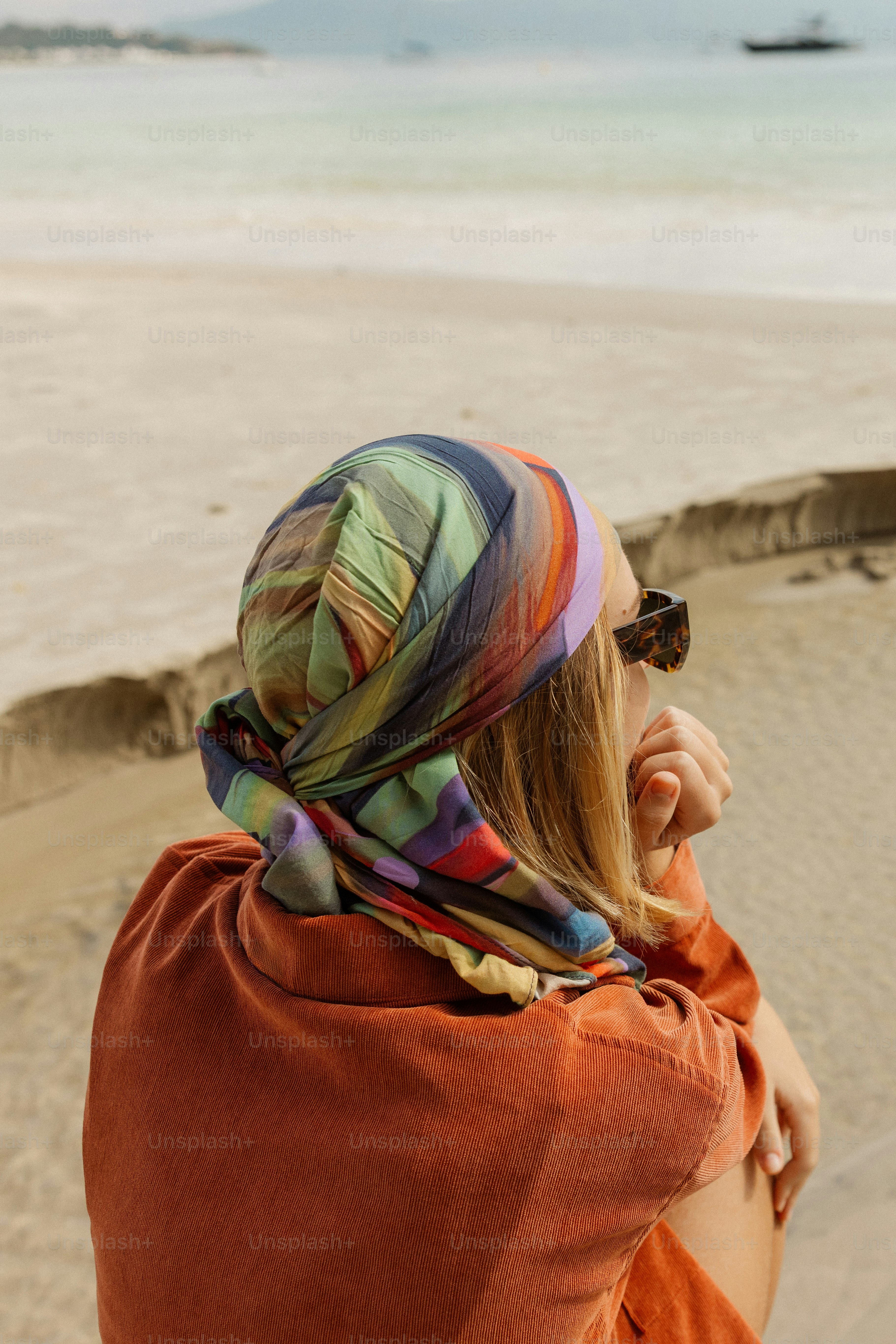 Woman wearing a colorful headscarf looking at a sandy beach.