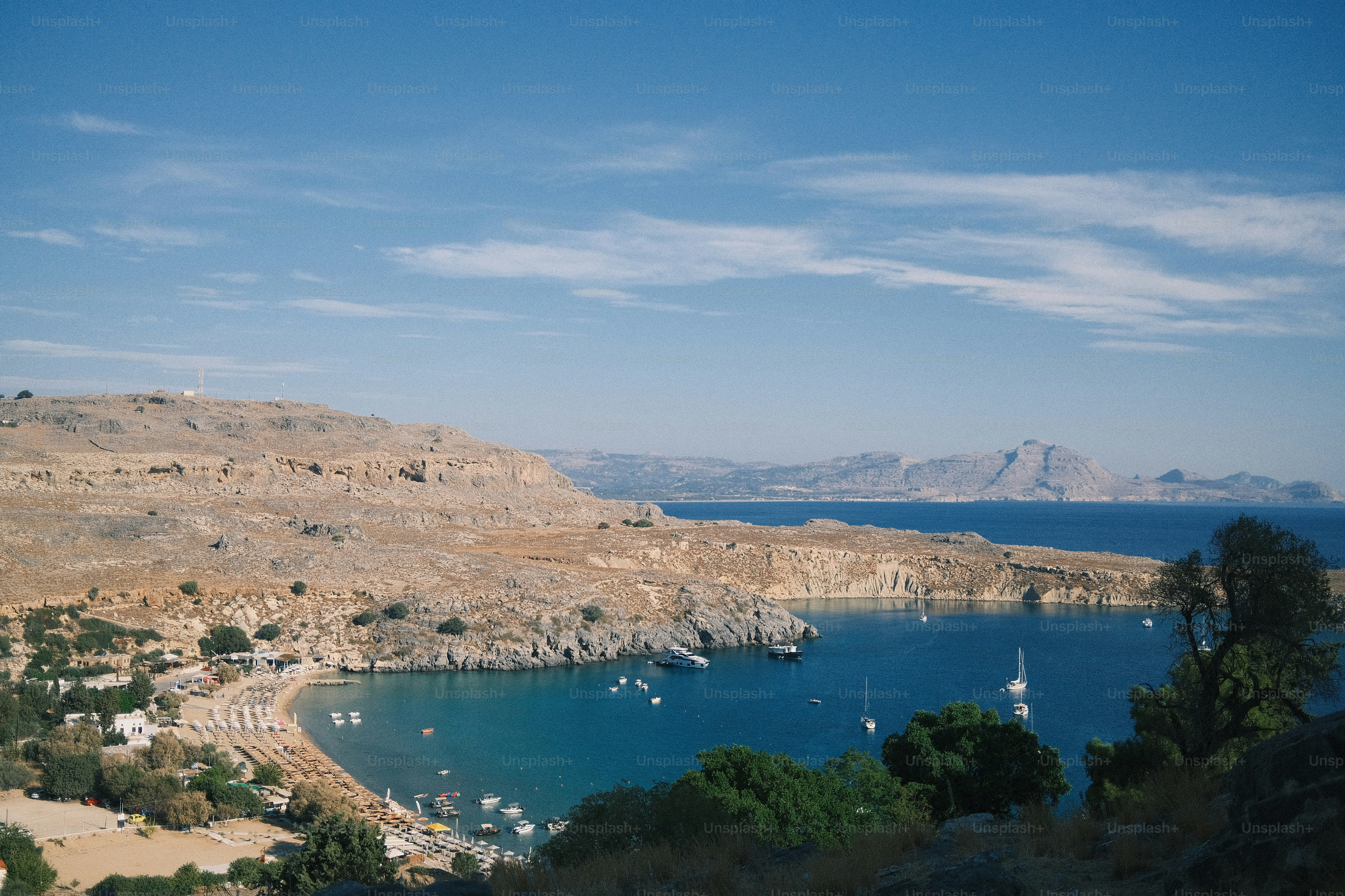Bahía azul clara con barcos y colinas costeras áridas.