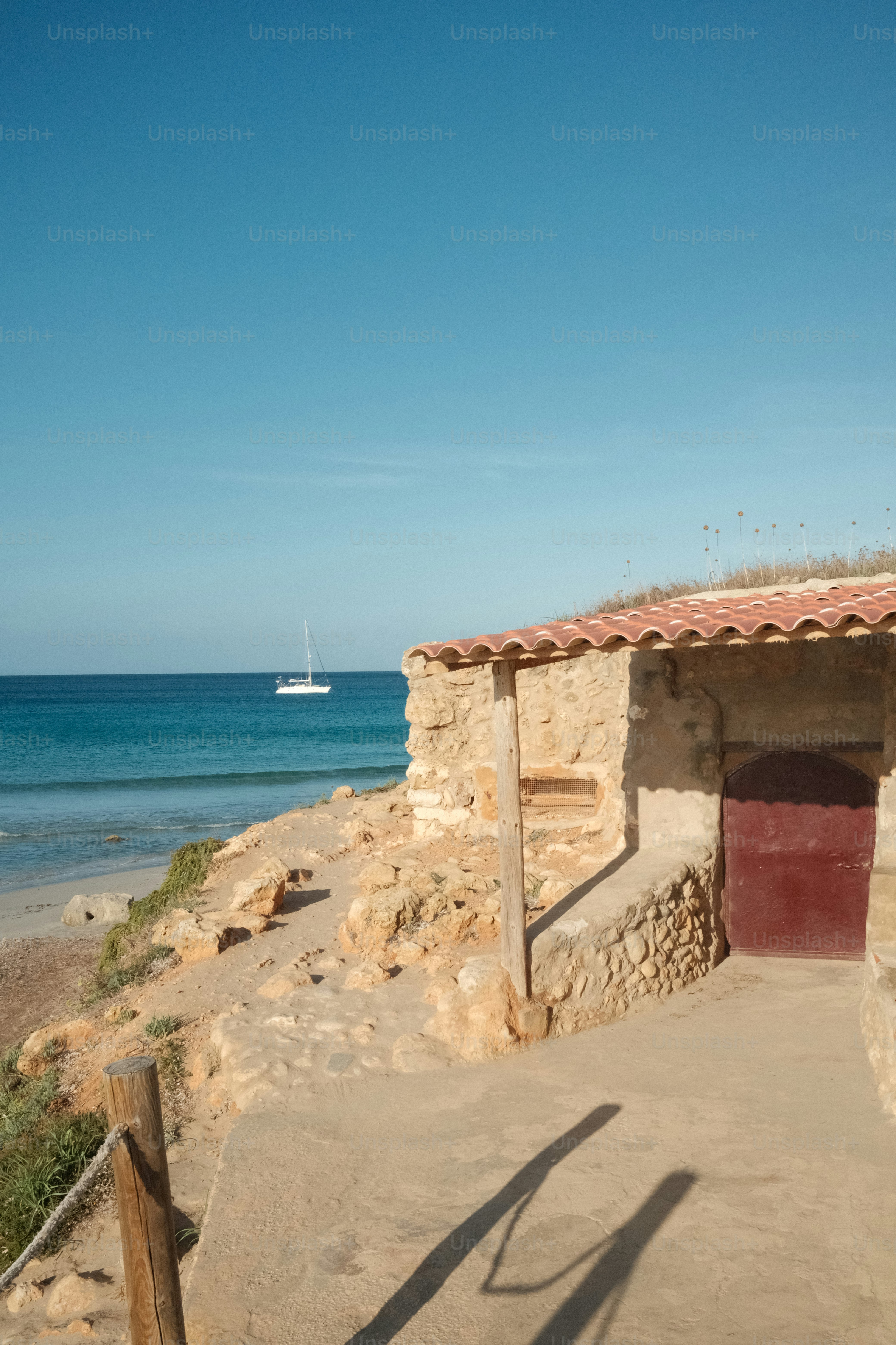 Antigua casa de piedra junto al mar con un velero lejano.
