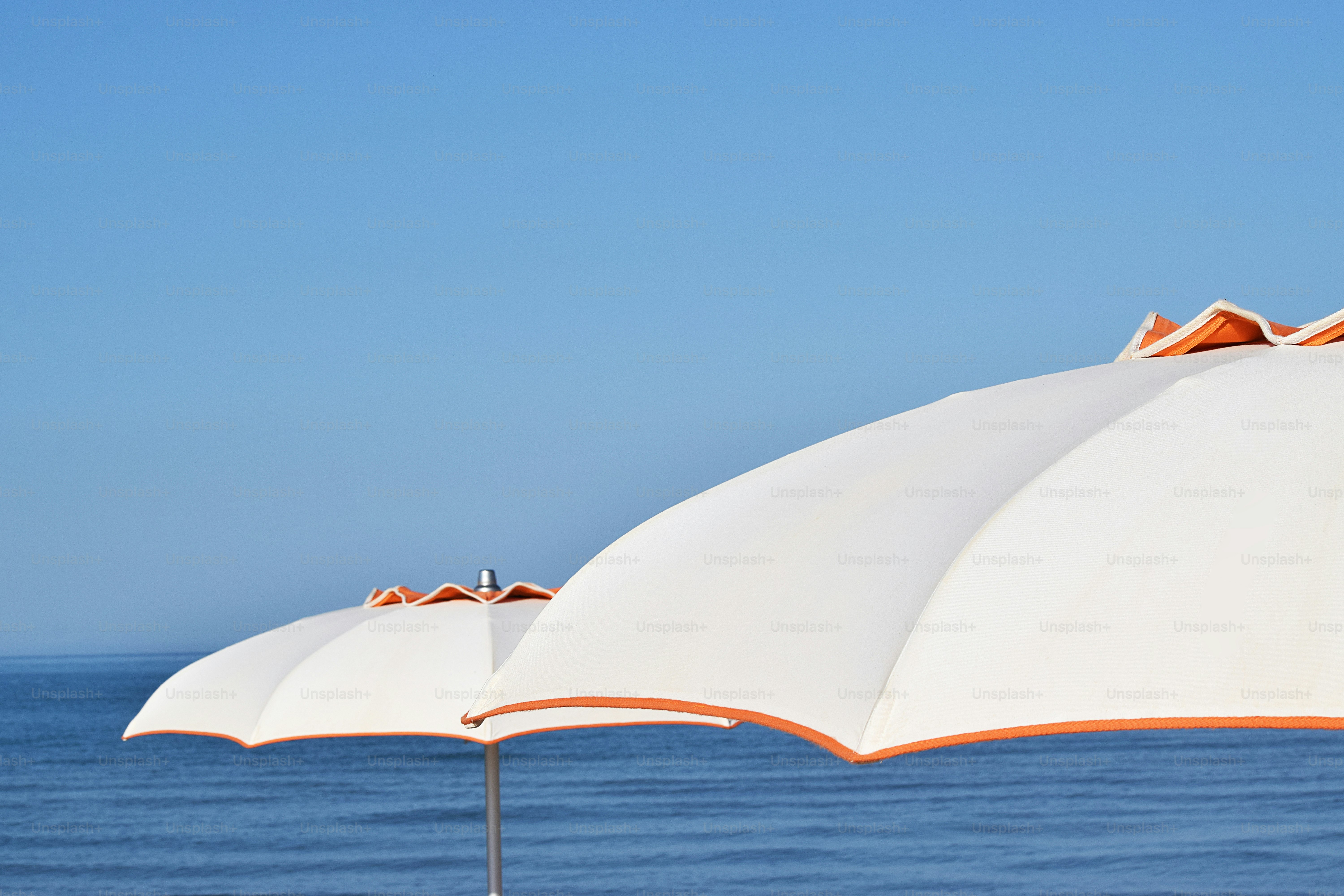 Two white beach umbrellas against a blue sky and ocean.