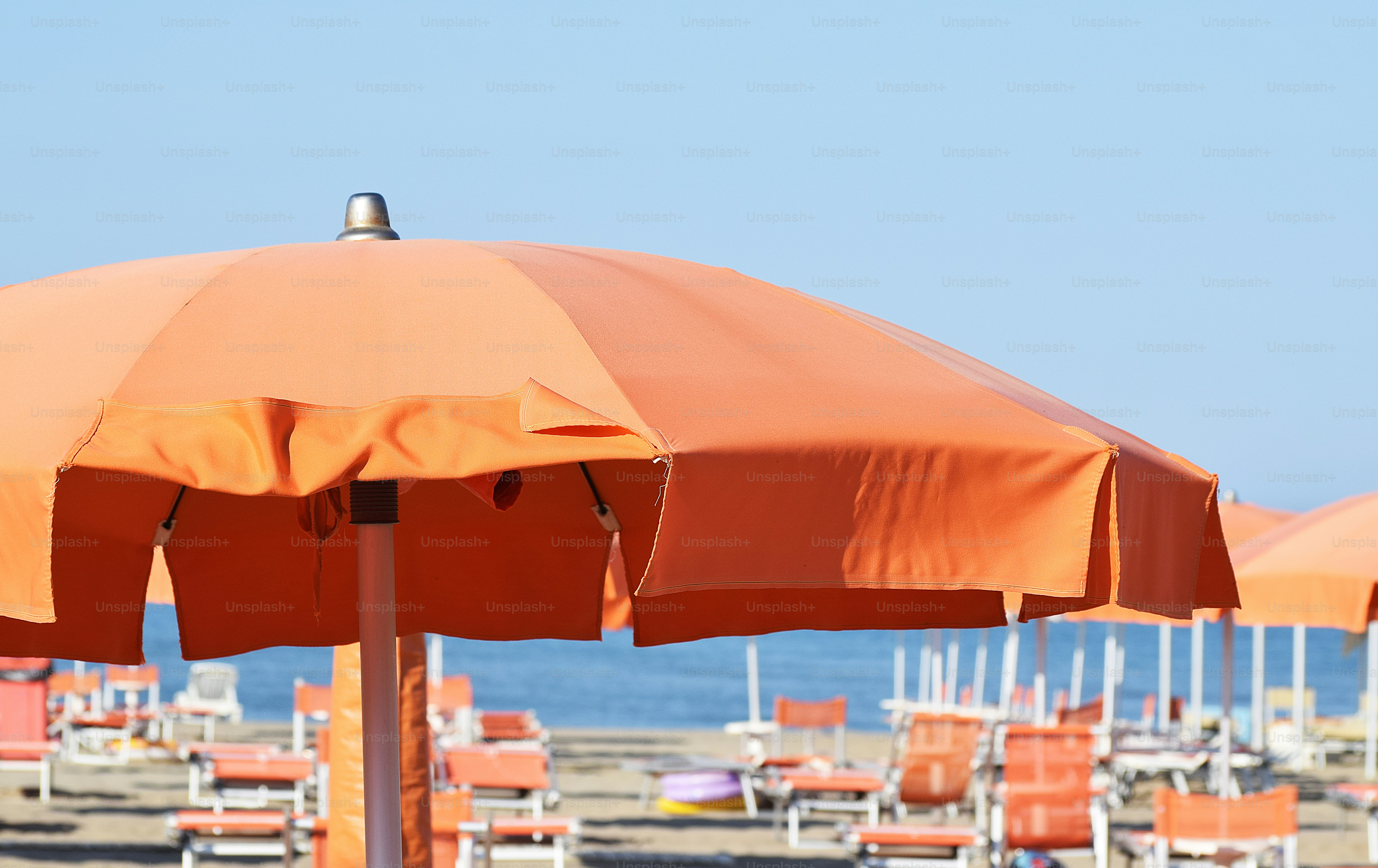 Orange beach umbrellas and chairs on a sunny beach.