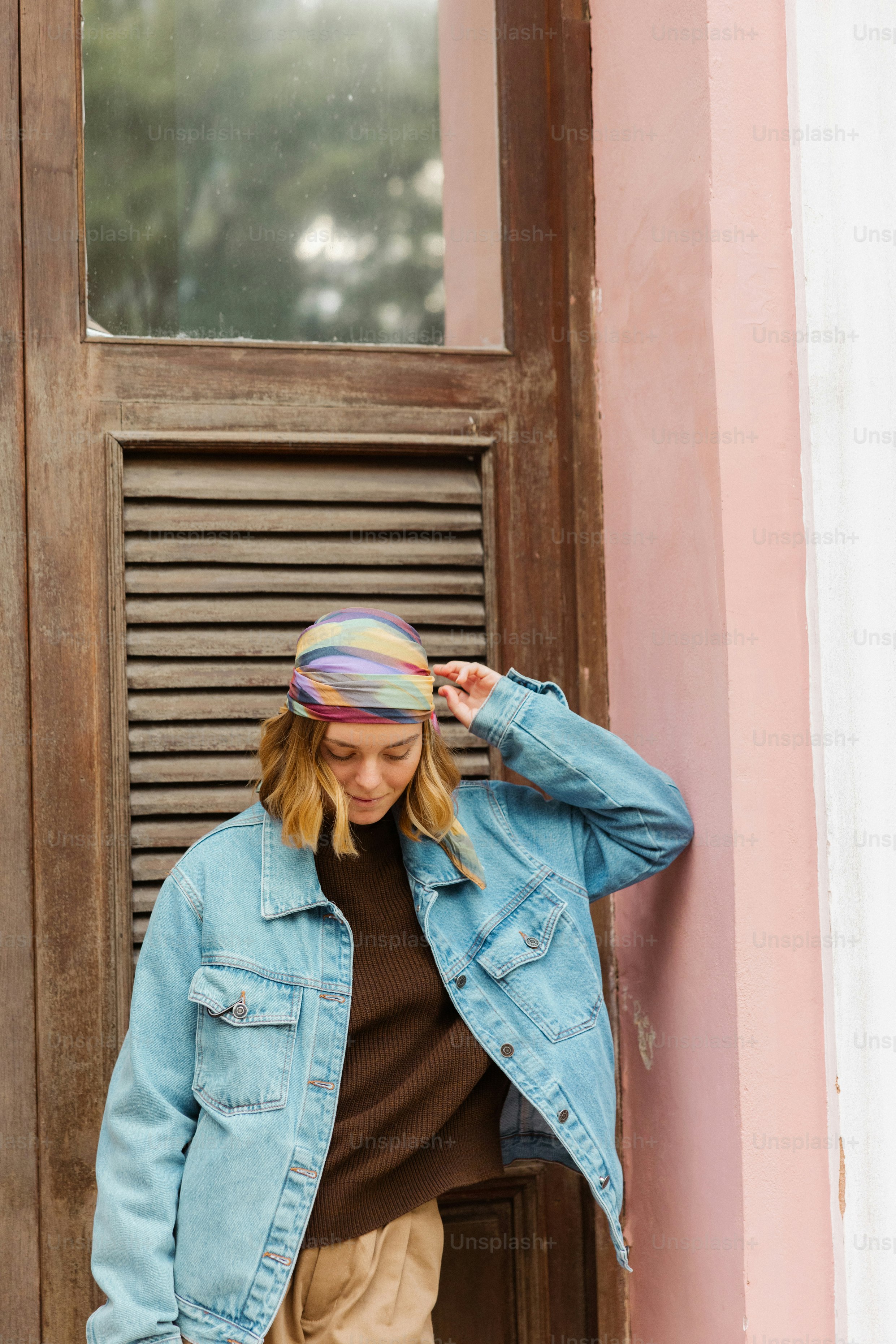 Frau in Jeansjacke und Kopftuch lehnt an die rosa Wand.