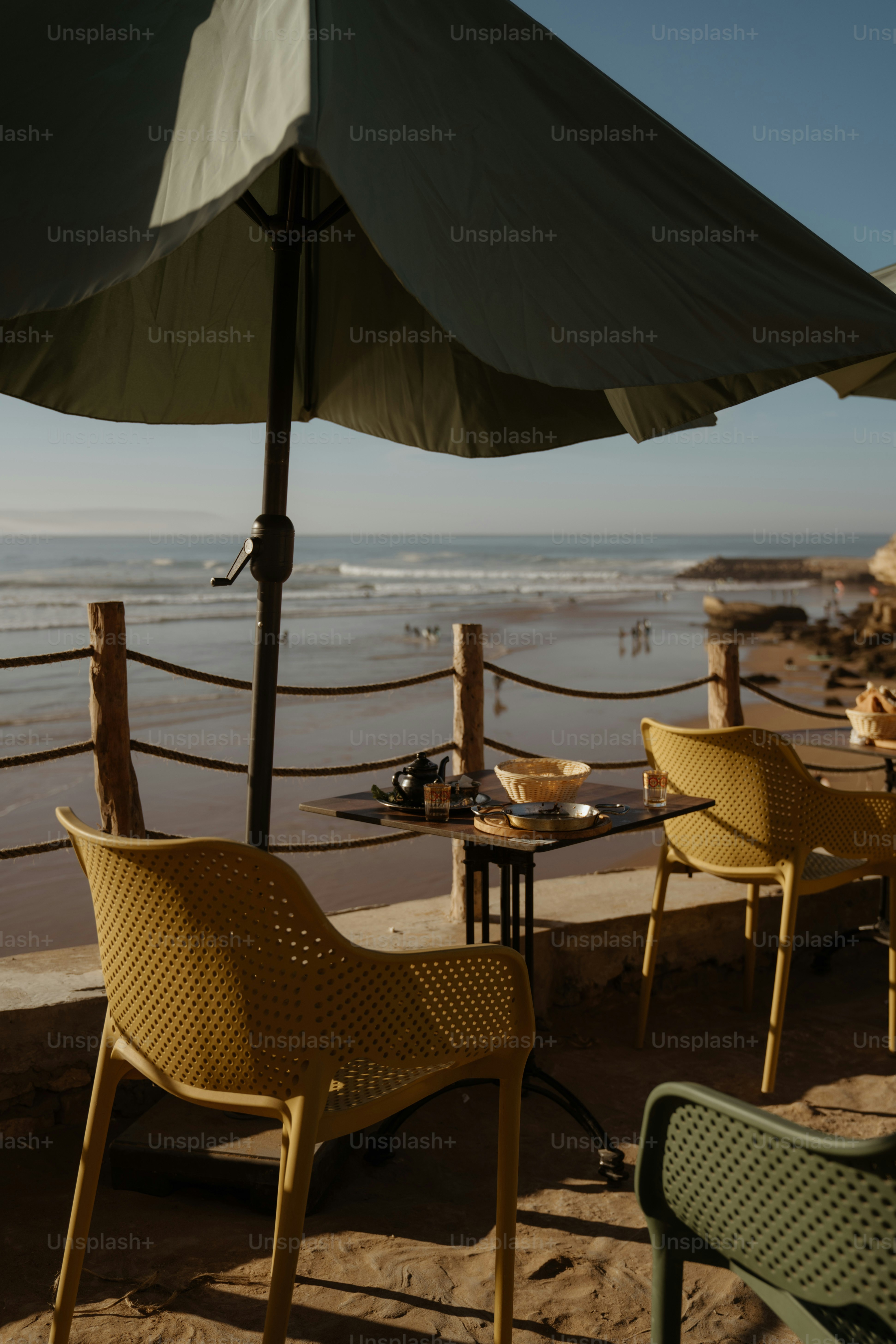 Pátio café com vista para uma praia ensolarada e ondas do mar.