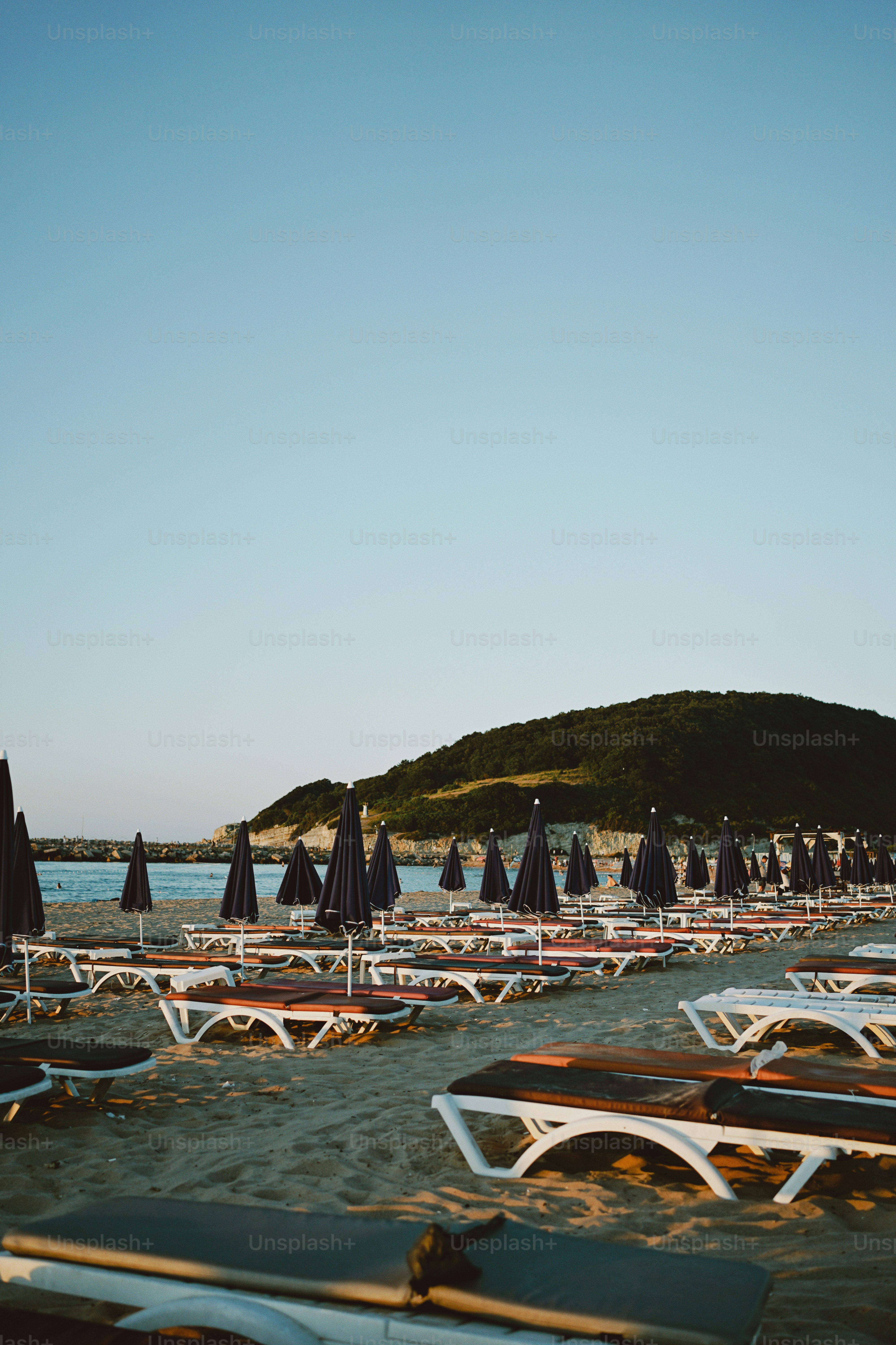 Strand mit Liegestühlen, Sonnenschirmen, Ozean und einem grünen Hügel