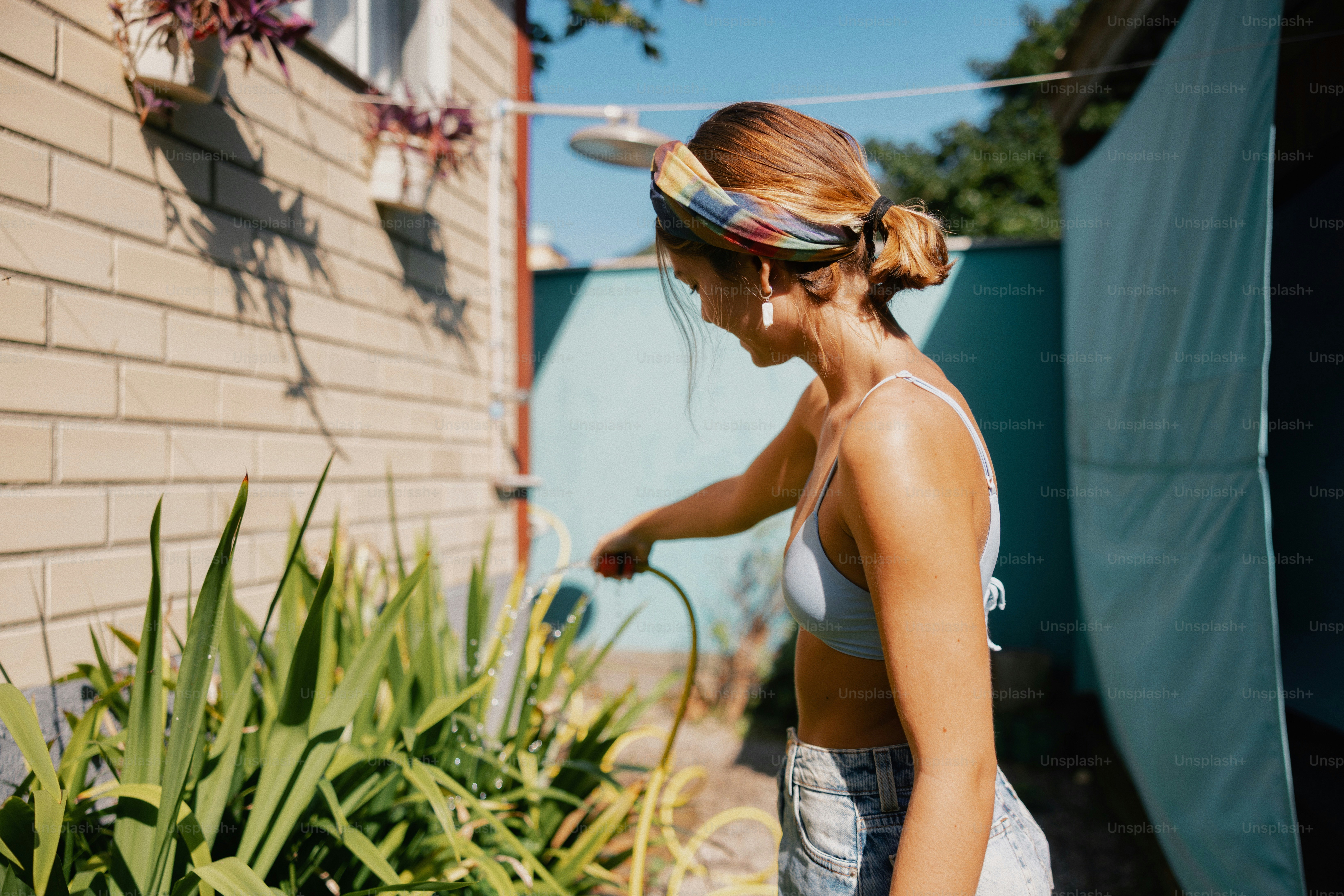 Woman in headscarf watering green plants outdoors.