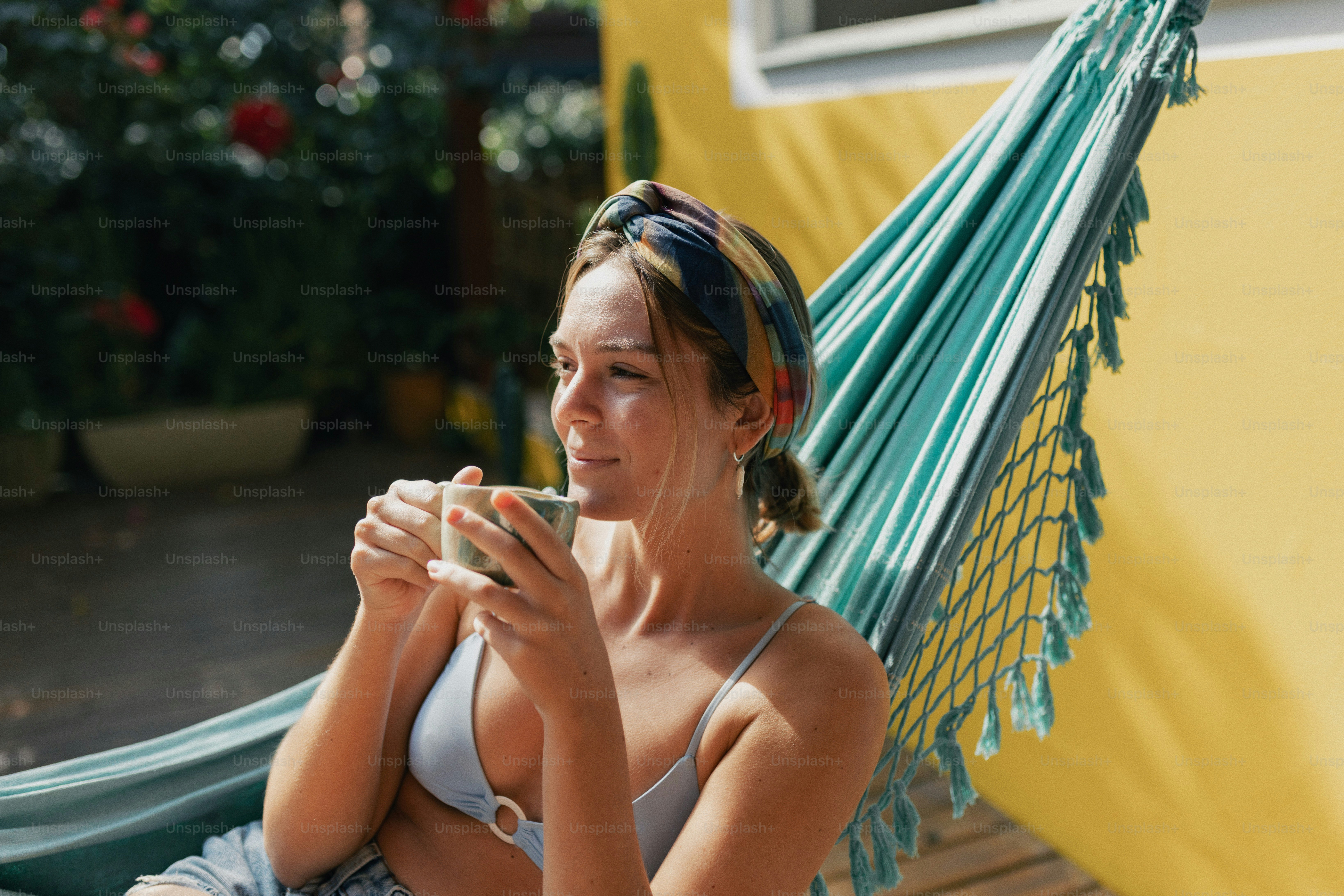 Relaxed woman enjoying a beverage in a vibrant turquoise hammock.