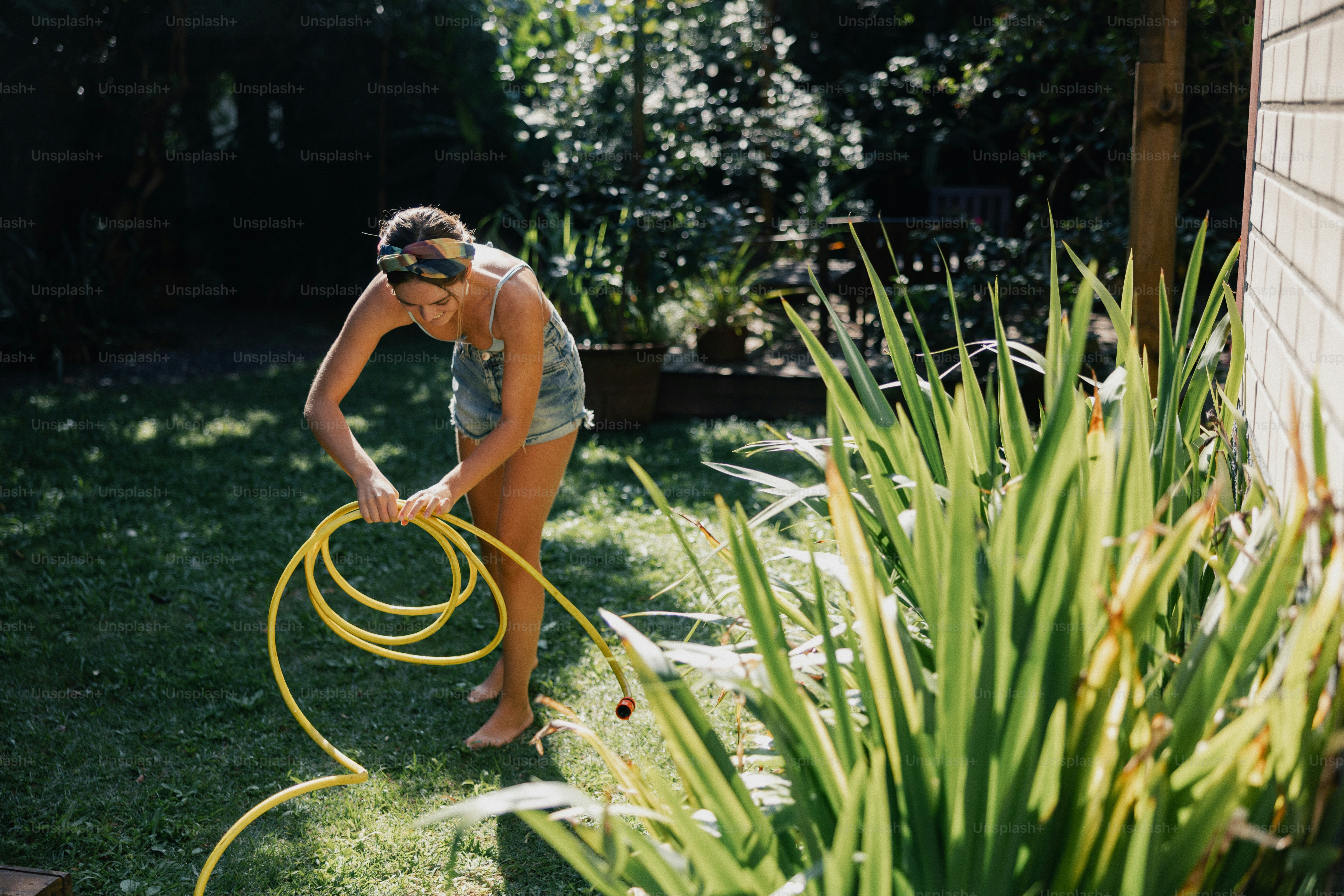 Woman coiling a yellow garden hose in a sunny garden.