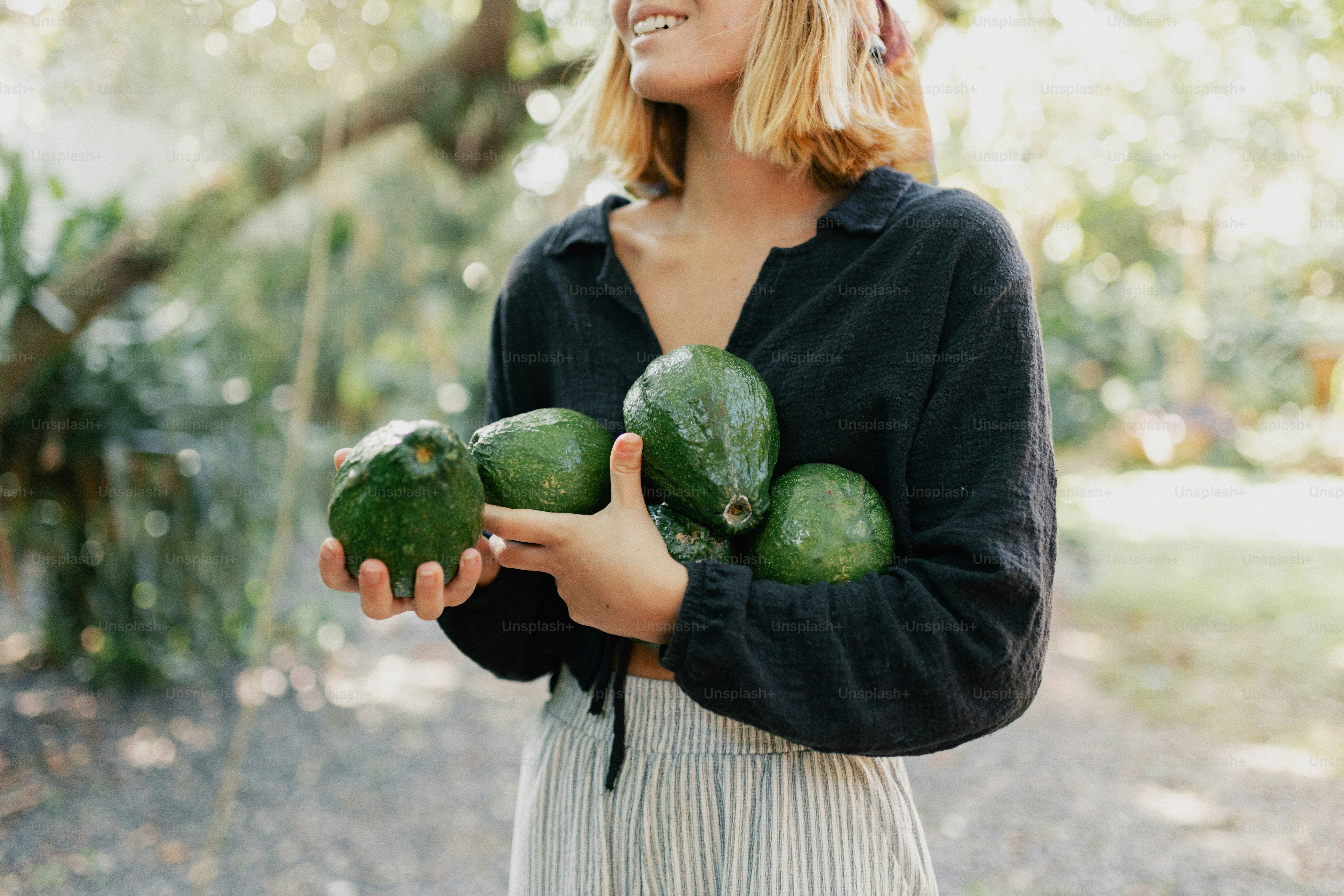 A young woman holding several fresh green avocados outdoors.