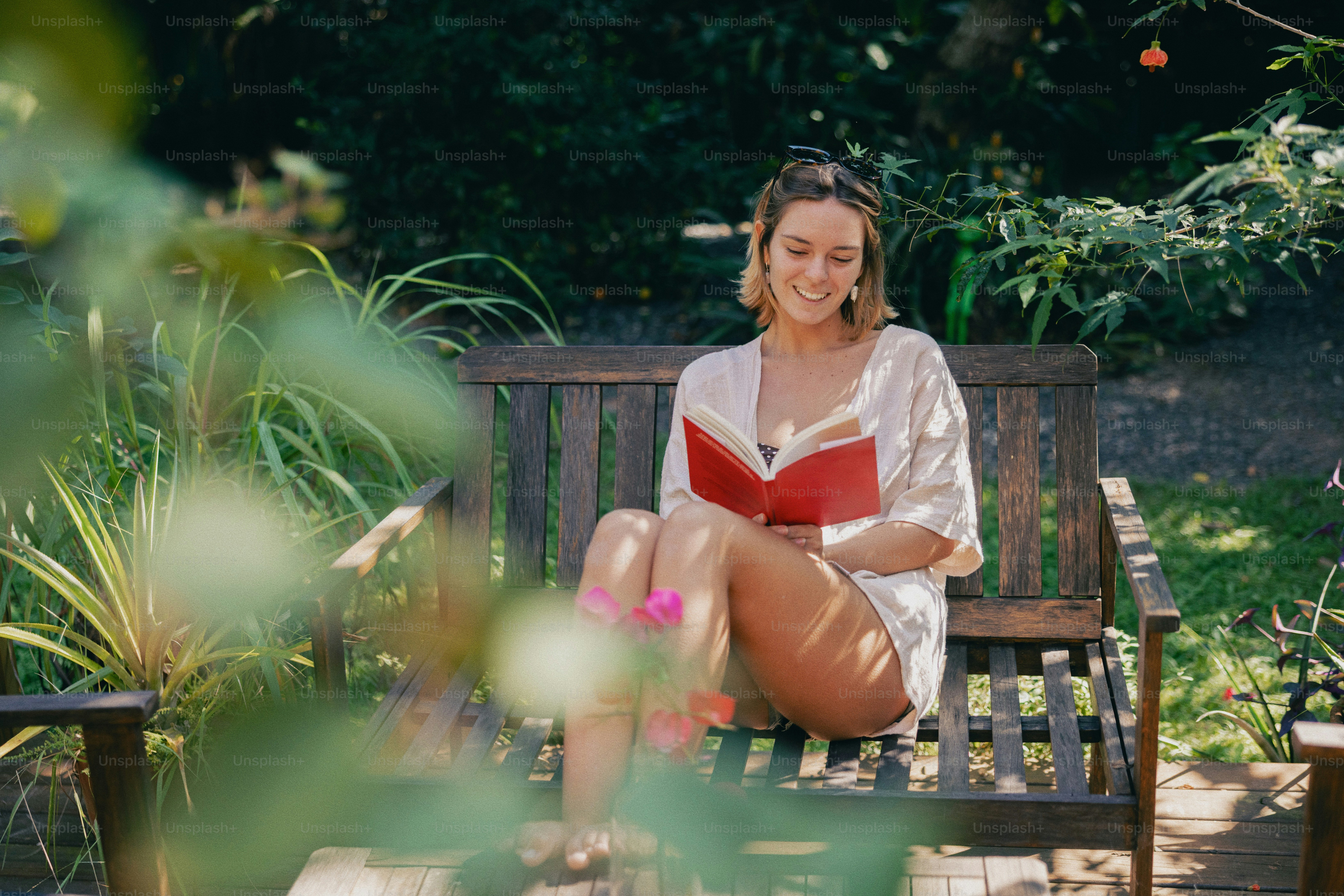 Smiling woman reads a book on a garden bench.
