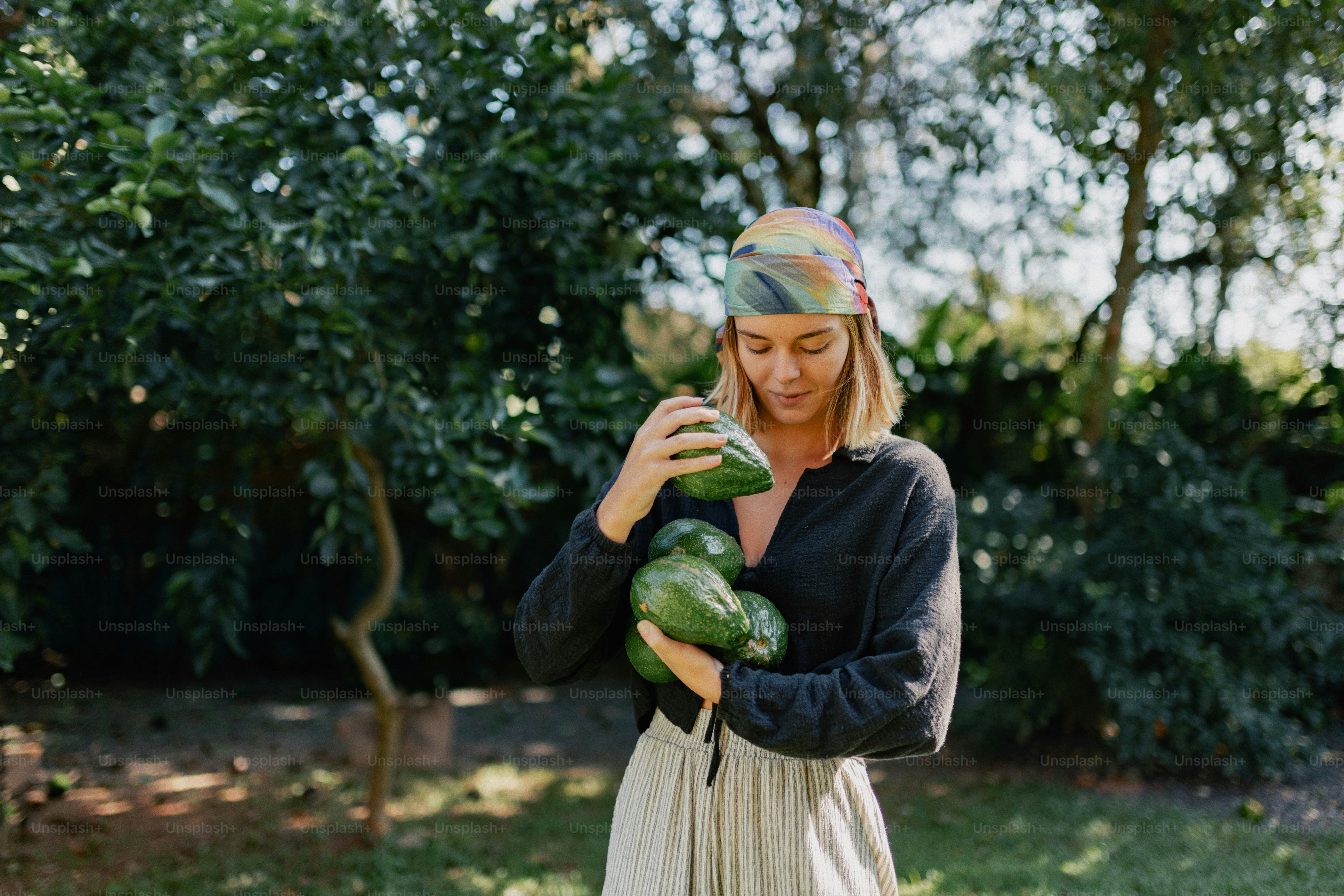 A woman holding several green avocados outdoors.
