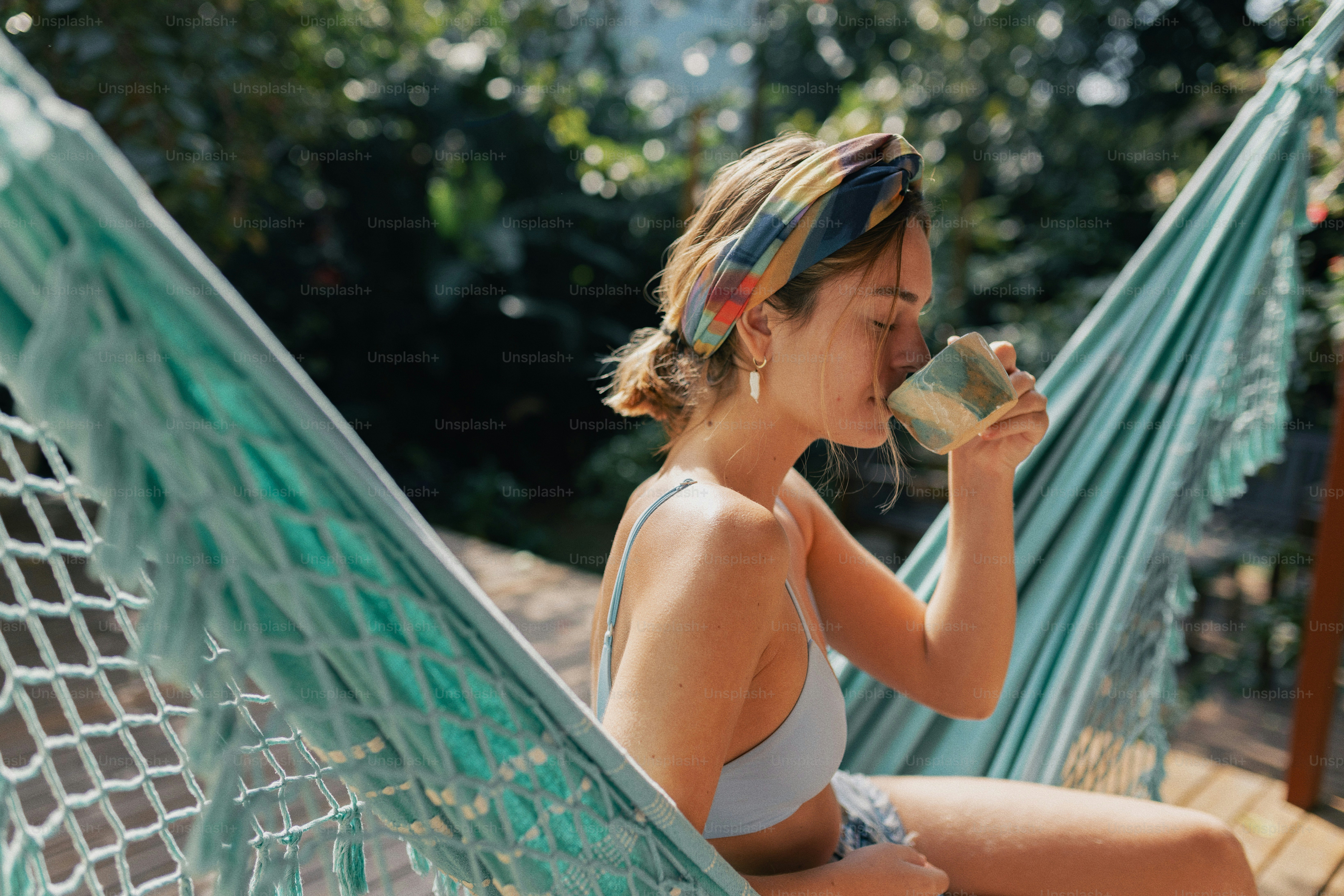 A woman relaxes in a hammock, drinking from a mug.