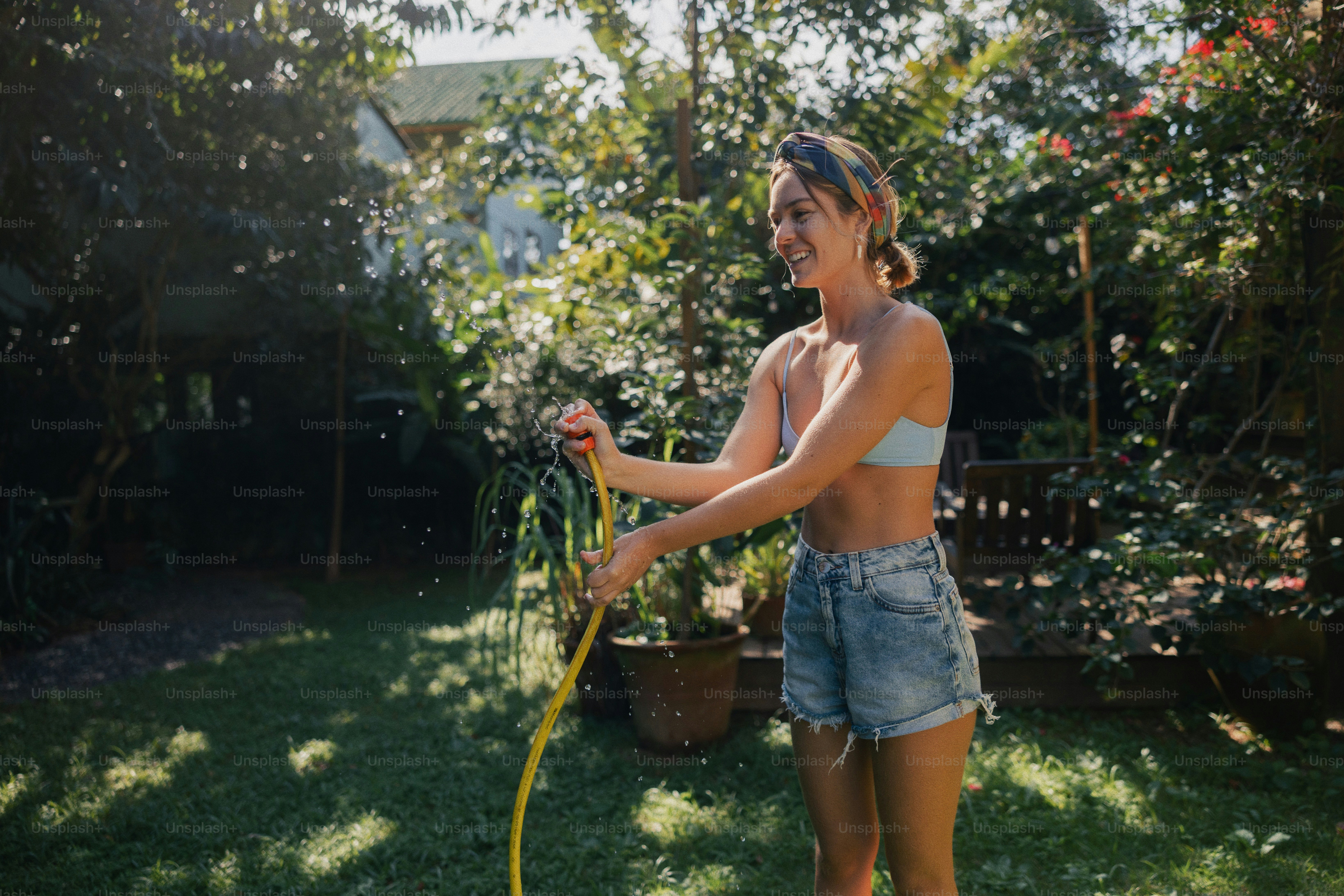 A smiling woman waters plants in a sunny garden.