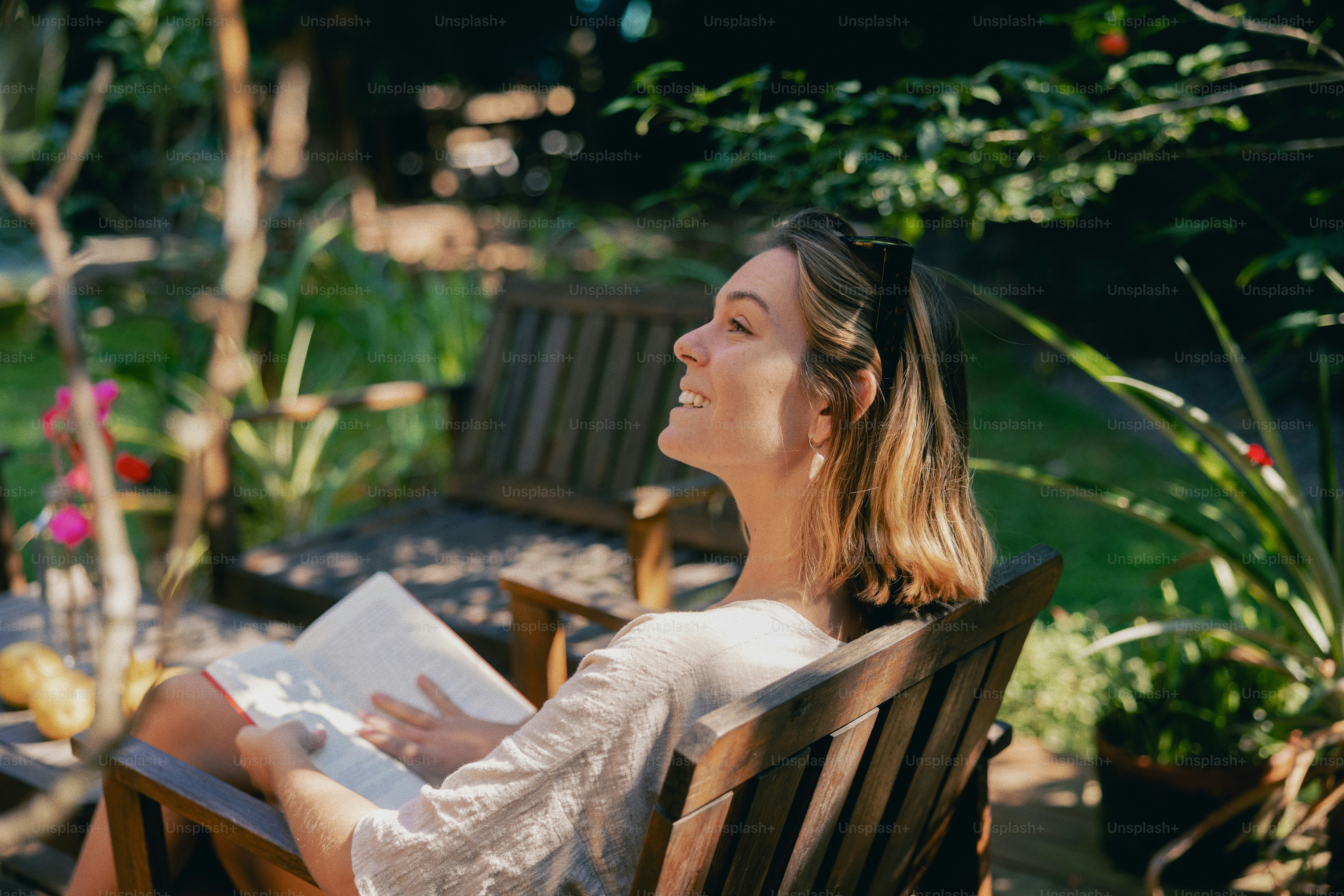 A woman reading a book outdoors in a sunny garden.
